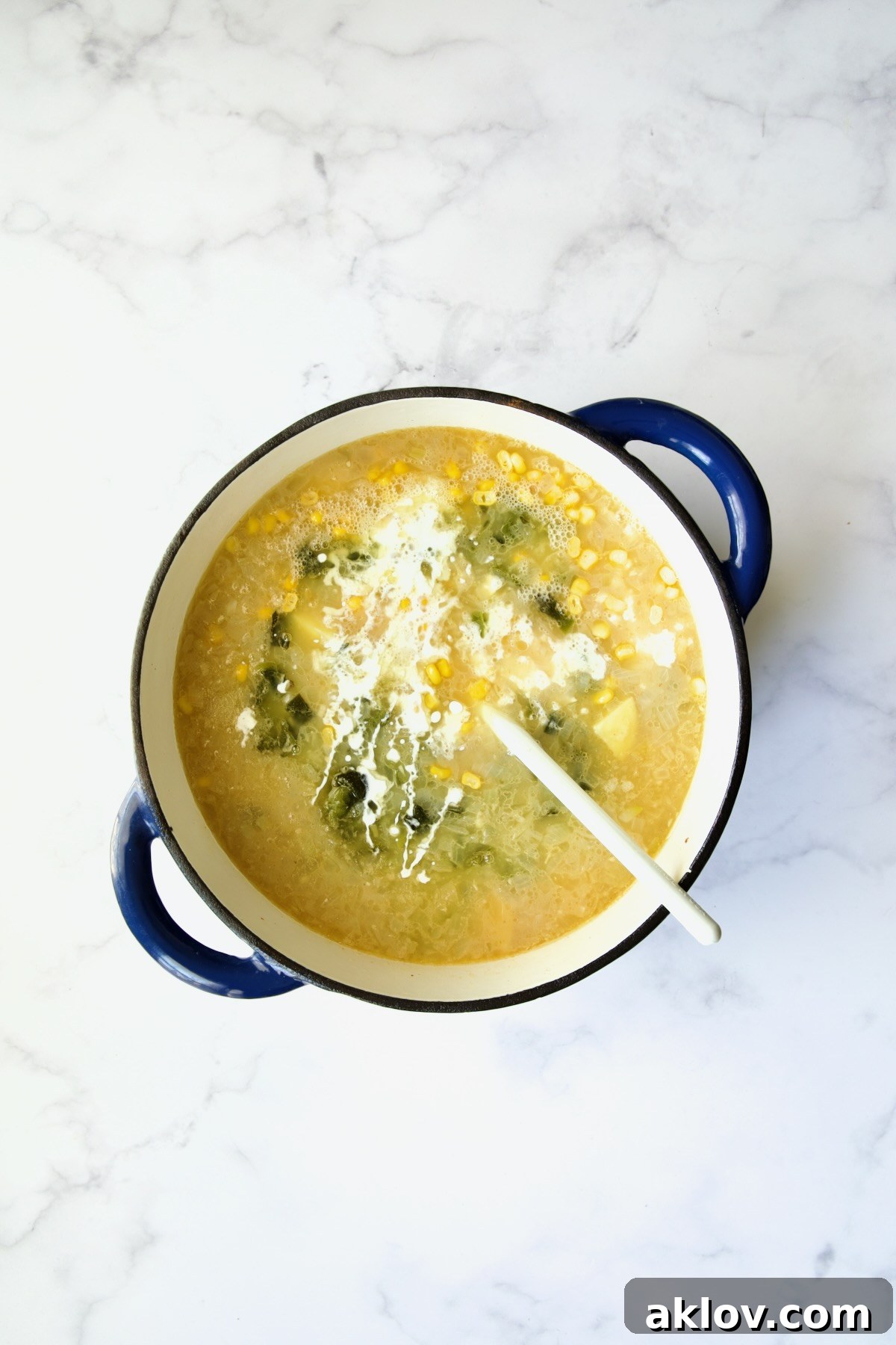 Sweet corn, smoky roasted poblanos, and rich heavy cream being gently stirred into the chowder base in a blue Dutch oven.