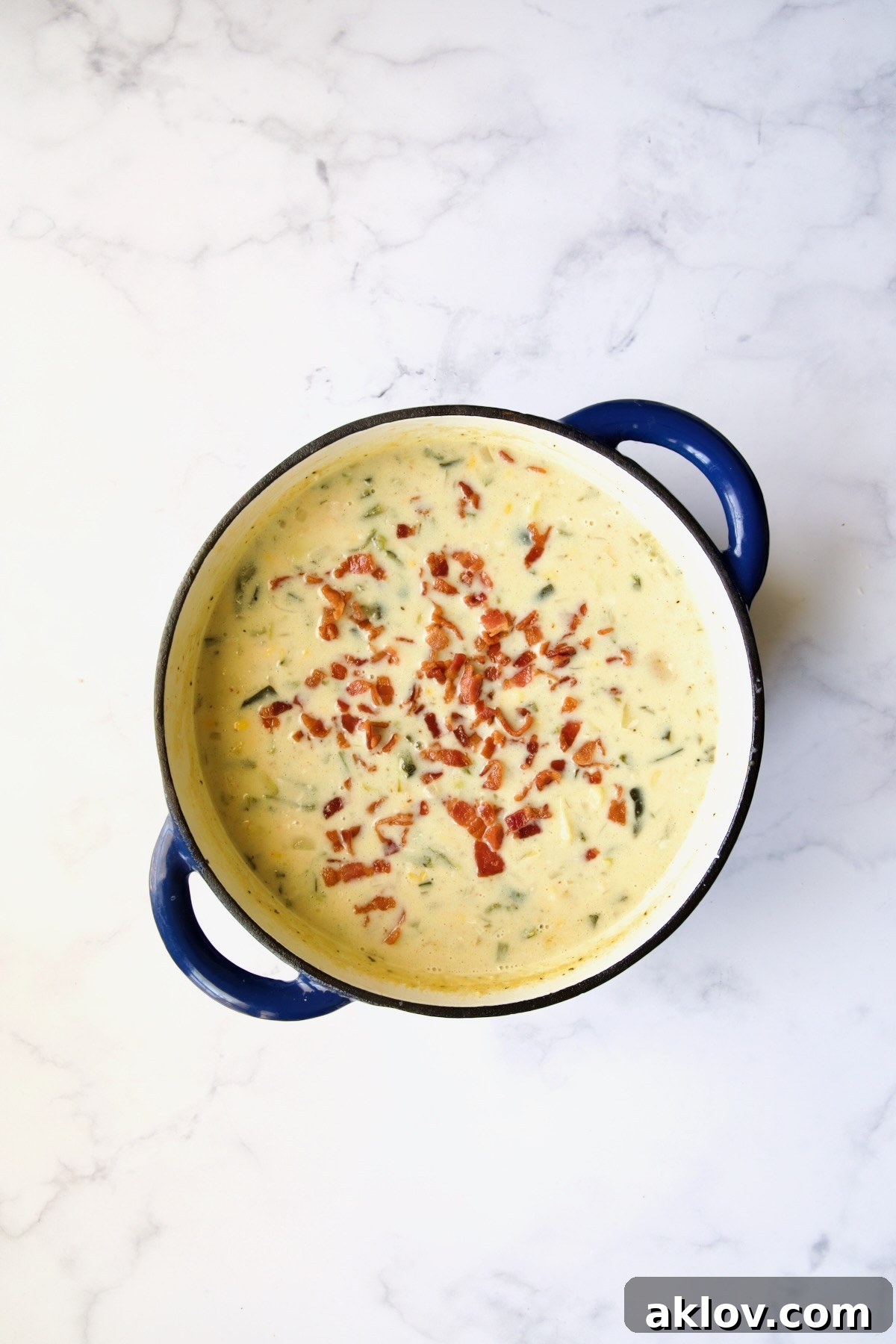 Crispy bacon pieces stirred into the rich, creamy chowder in a blue Dutch oven, adding a savory depth.
