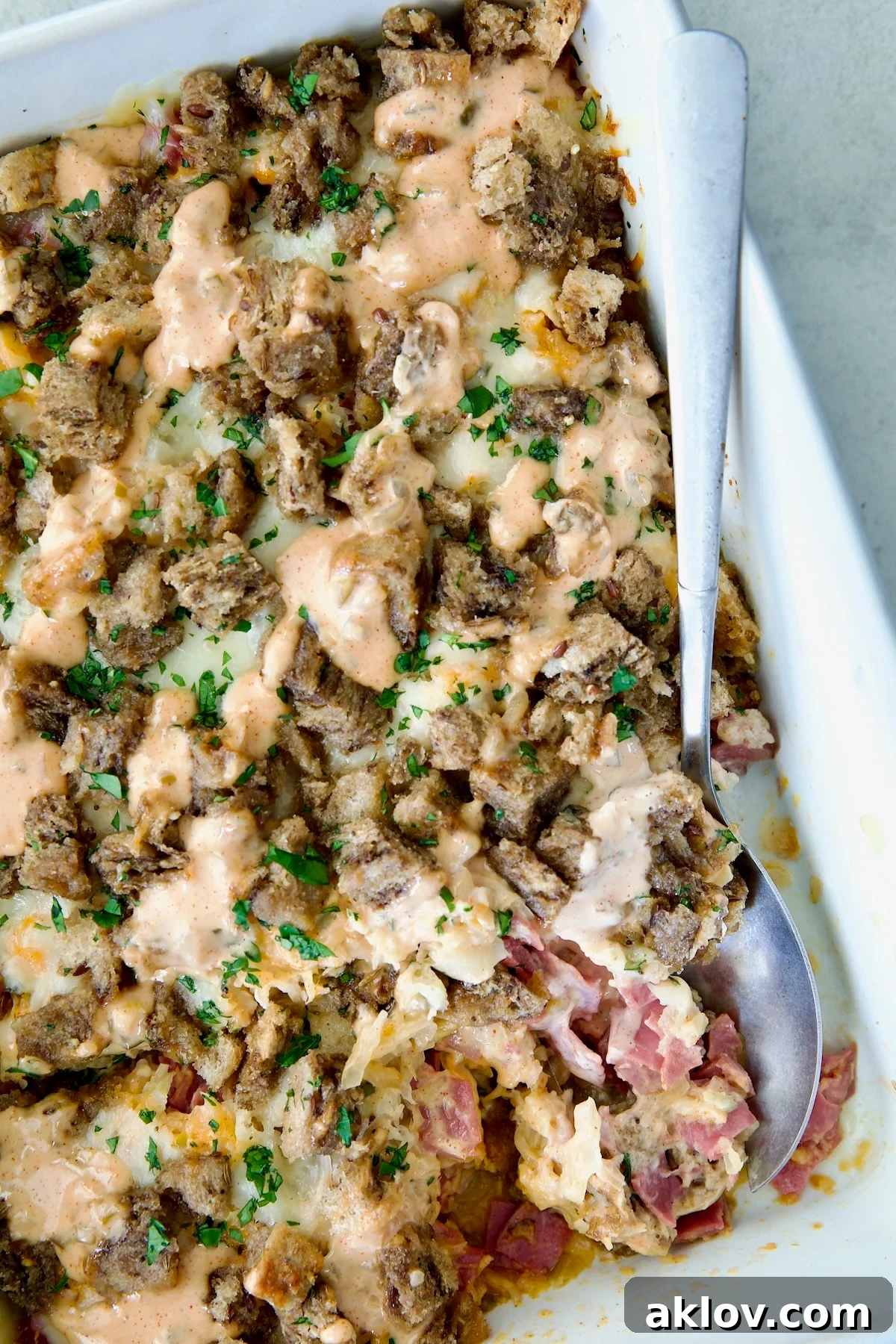 Creamy Reuben Comfort Casserole 18 A serving spoon lifting a portion of the delicious Reuben Casserole from the white rectangular baking dish, steam gently rising.