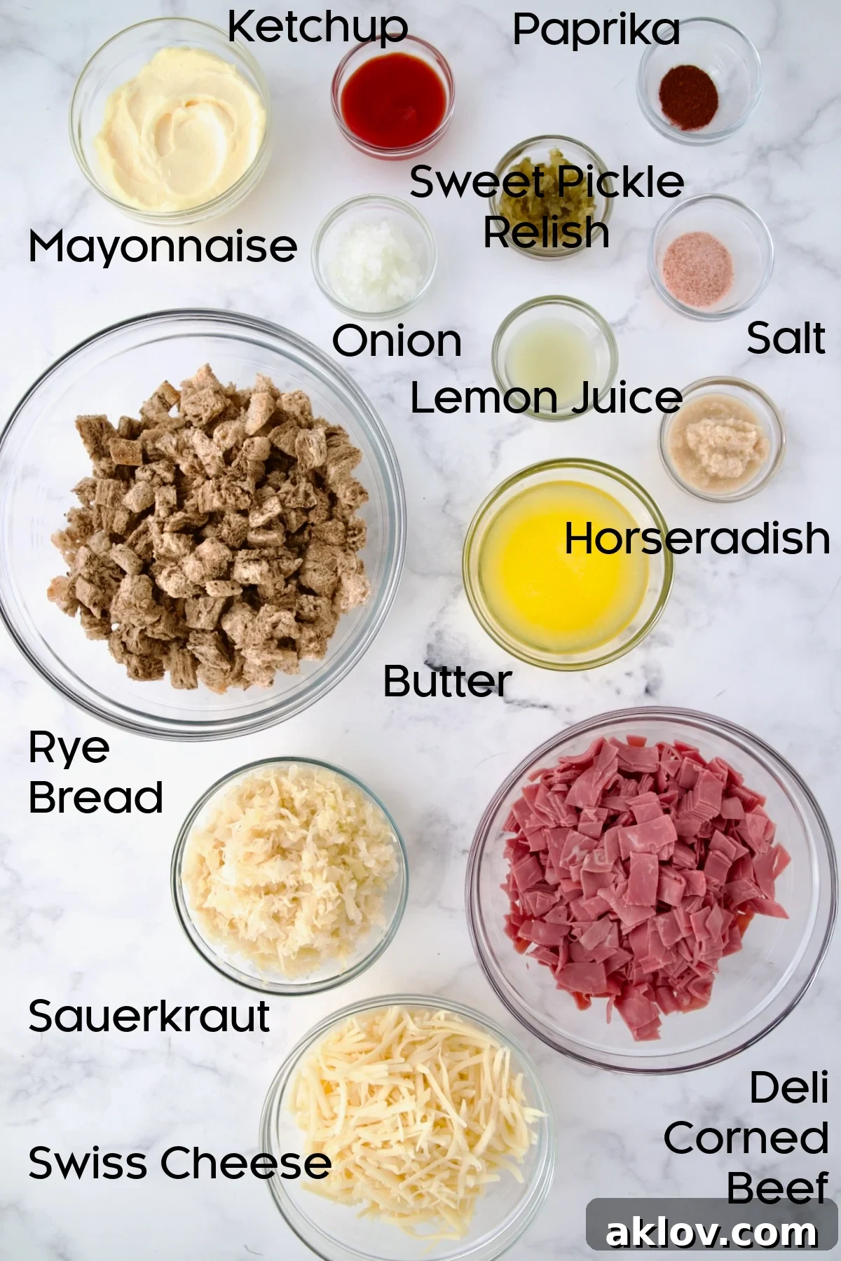 Creamy Reuben Comfort Casserole 4 Various ingredients for Reuben Casserole neatly arranged in clear glass bowls, including mayonnaise, ketchup, relish, onion, lemon, paprika, horseradish, corned beef, sauerkraut, Swiss cheese, butter, and rye bread cubes.