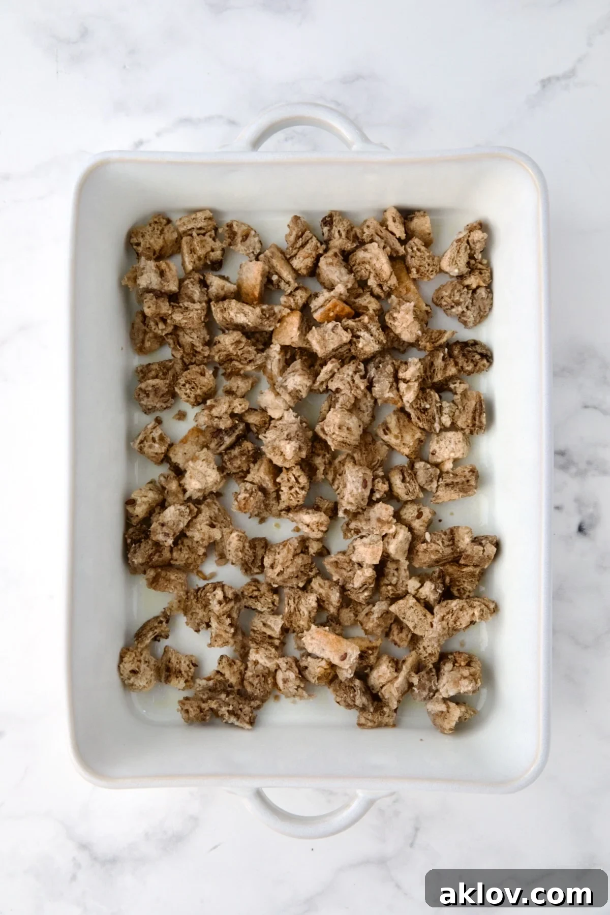 Creamy Reuben Comfort Casserole 8 Buttered rye bread cubes forming the initial layer in a white rectangular baking dish, ready for baking.