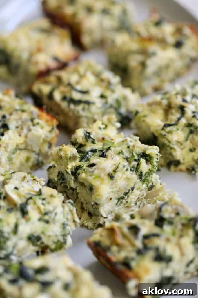 Close-up photo of baked Spinach Artichoke Squares cooling on a white platter, showing their inviting texture.