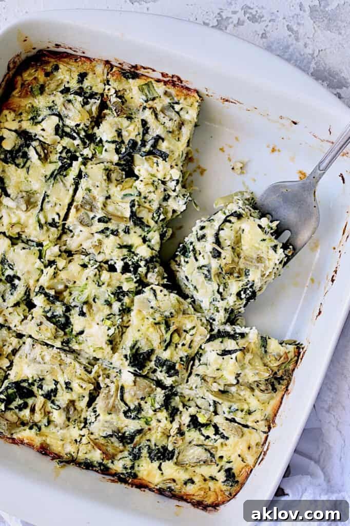 Photo of Spinach Artichoke Squares in white square baking dish cut into squares with serving fork.