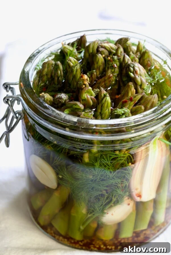 Asparagus with brine poured over it in glass jar.
