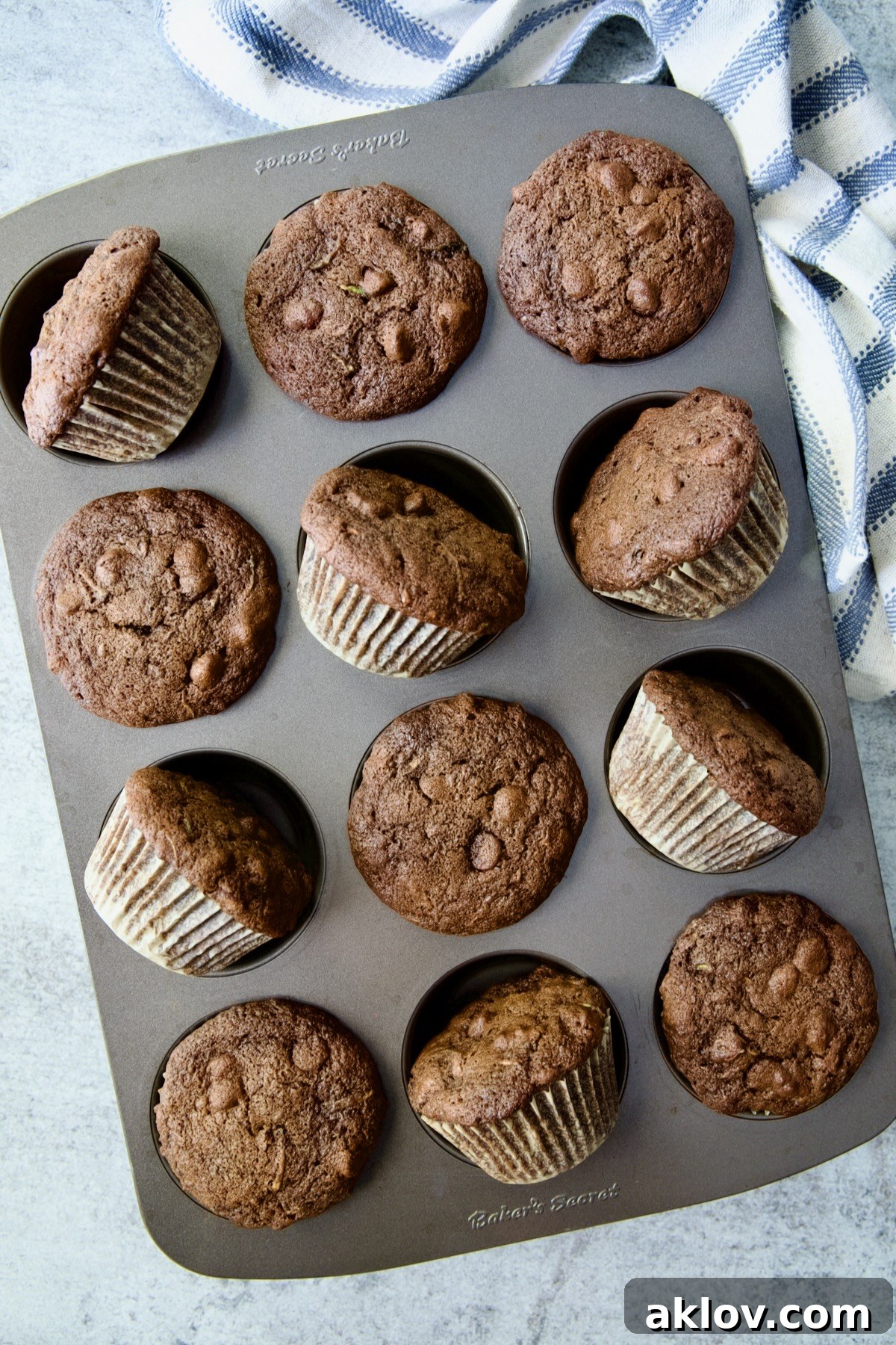 A batch of baked Chocolate and Zucchini Muffins, some turned on their sides, cooling in a 12-cup muffin pan.