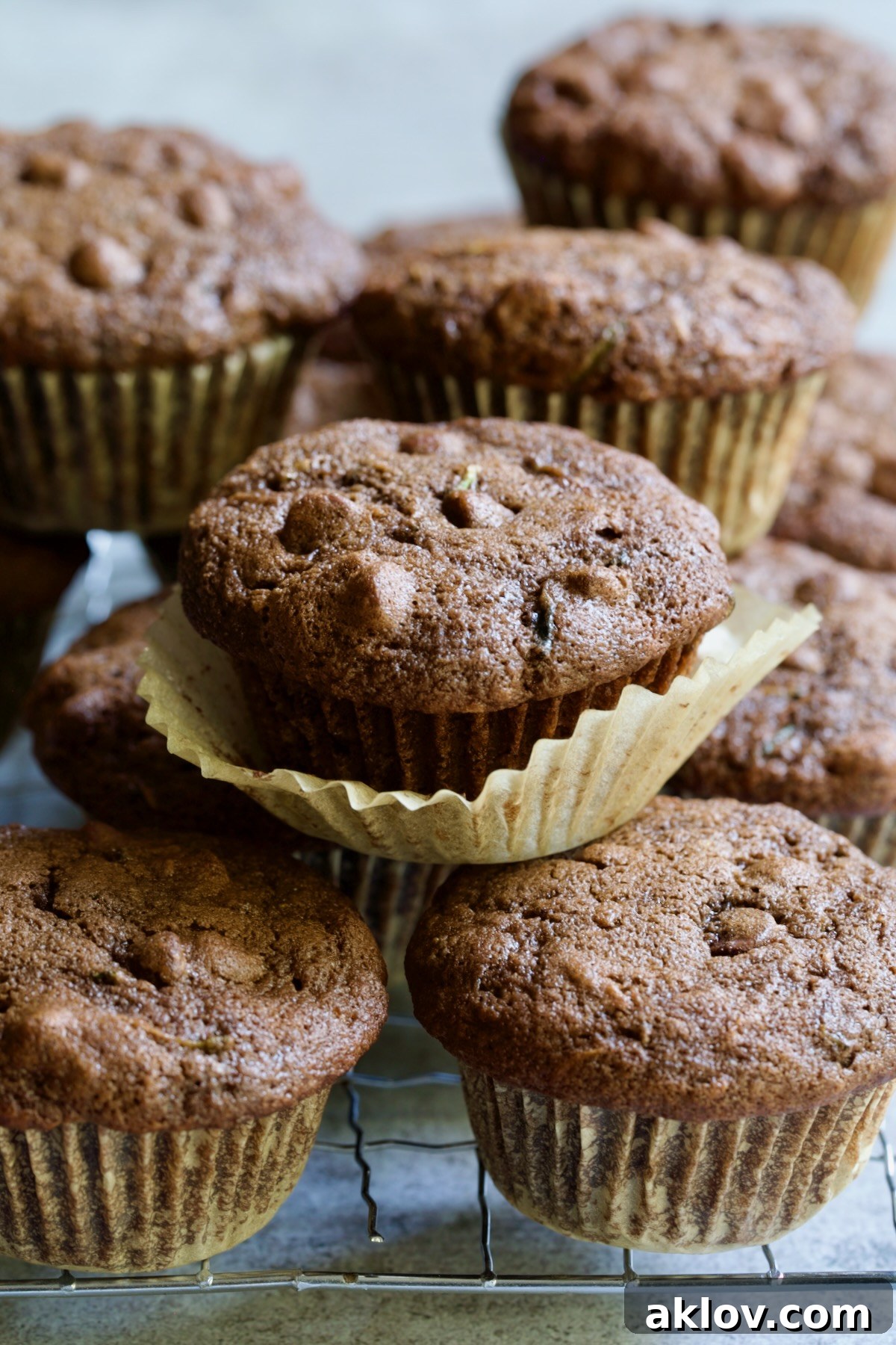Pile of Chocolate and Zucchini Muffins on cooling rack with paper liner pulled away from one of them.