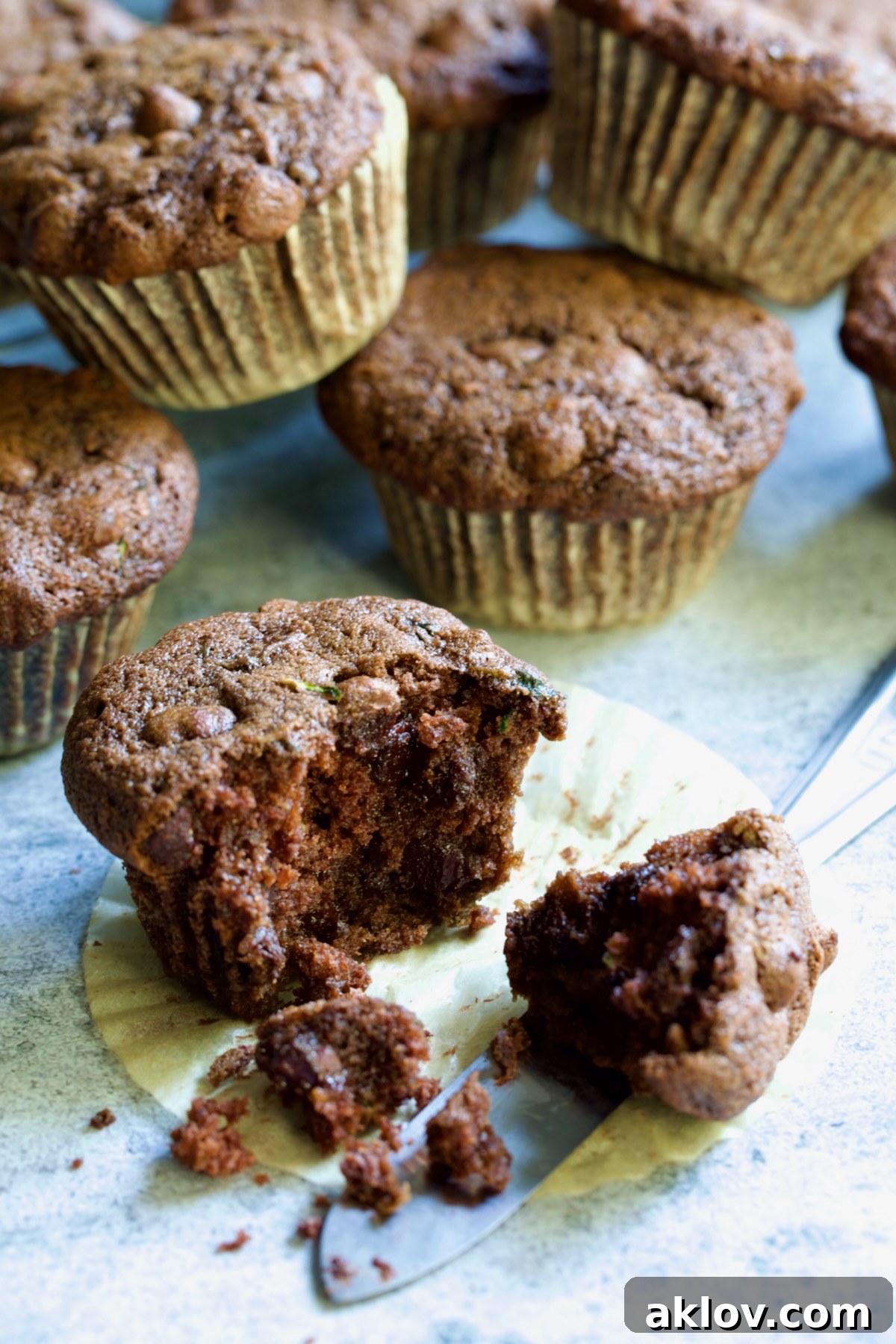 Half a Chocolate and Zucchini Muffin on paper muffin pan liner with table knife.