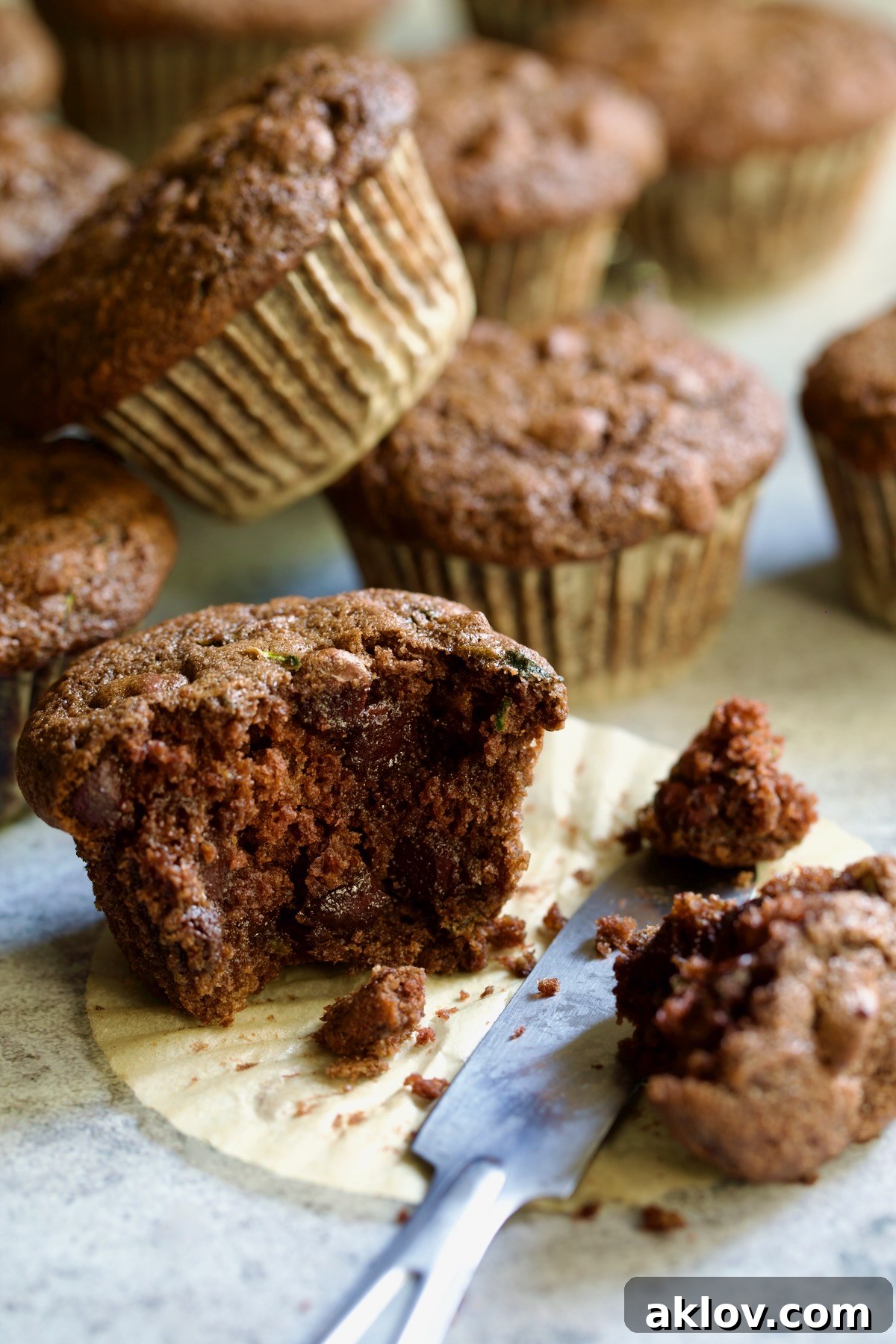 Half a Chocolate and Zucchini Muffin on paper muffin pan liner with table knife.