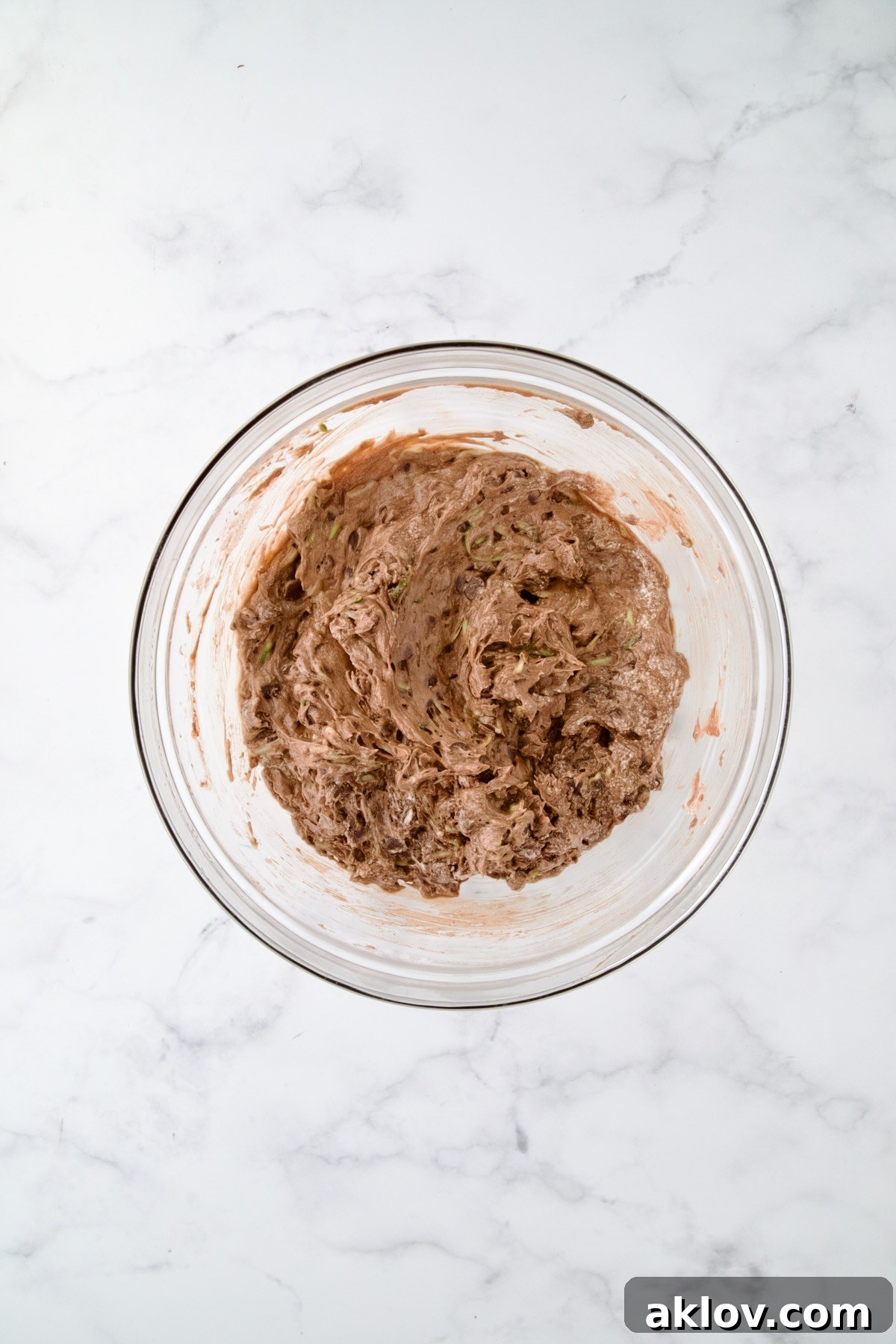 Chocolate muffin batter, with shredded zucchini and chocolate chips folded in, ready for baking in a glass bowl.