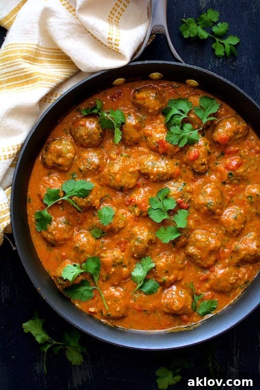 Photo of Meatballs in Spicy Curry smothered in sauce in skillet garnished with cilantro sprigs.