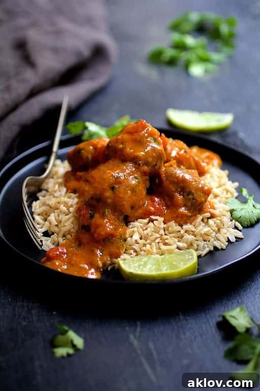 Photo of Meatballs in Spicy Curry over basmati rice on black plate garnished with lime. wedges and cilantro sprigs