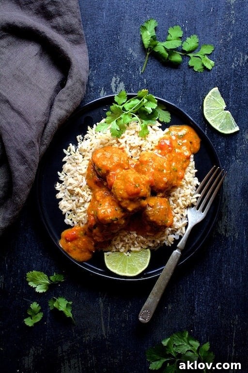 Photo of Meatballs in Spicy Curry over rice on black plate.