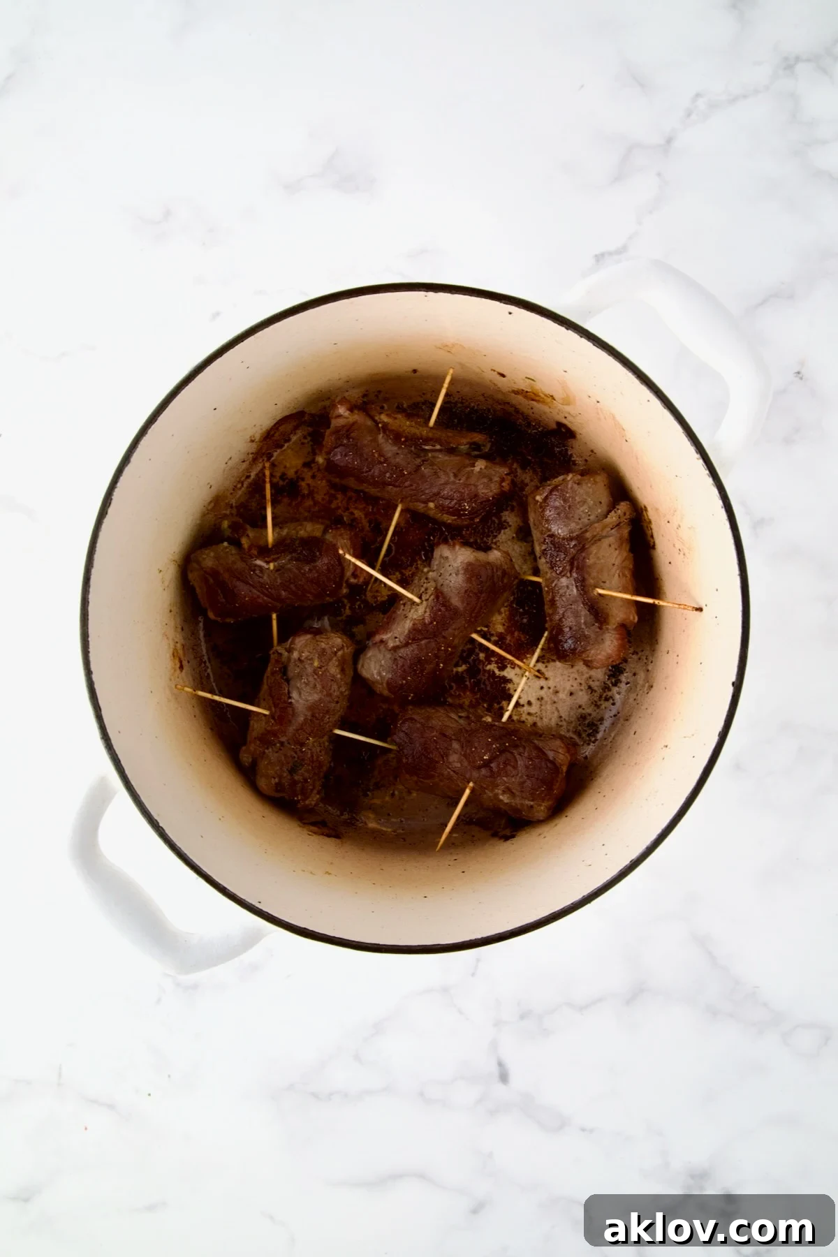Six beef rolls in white Dutch oven after being browned.