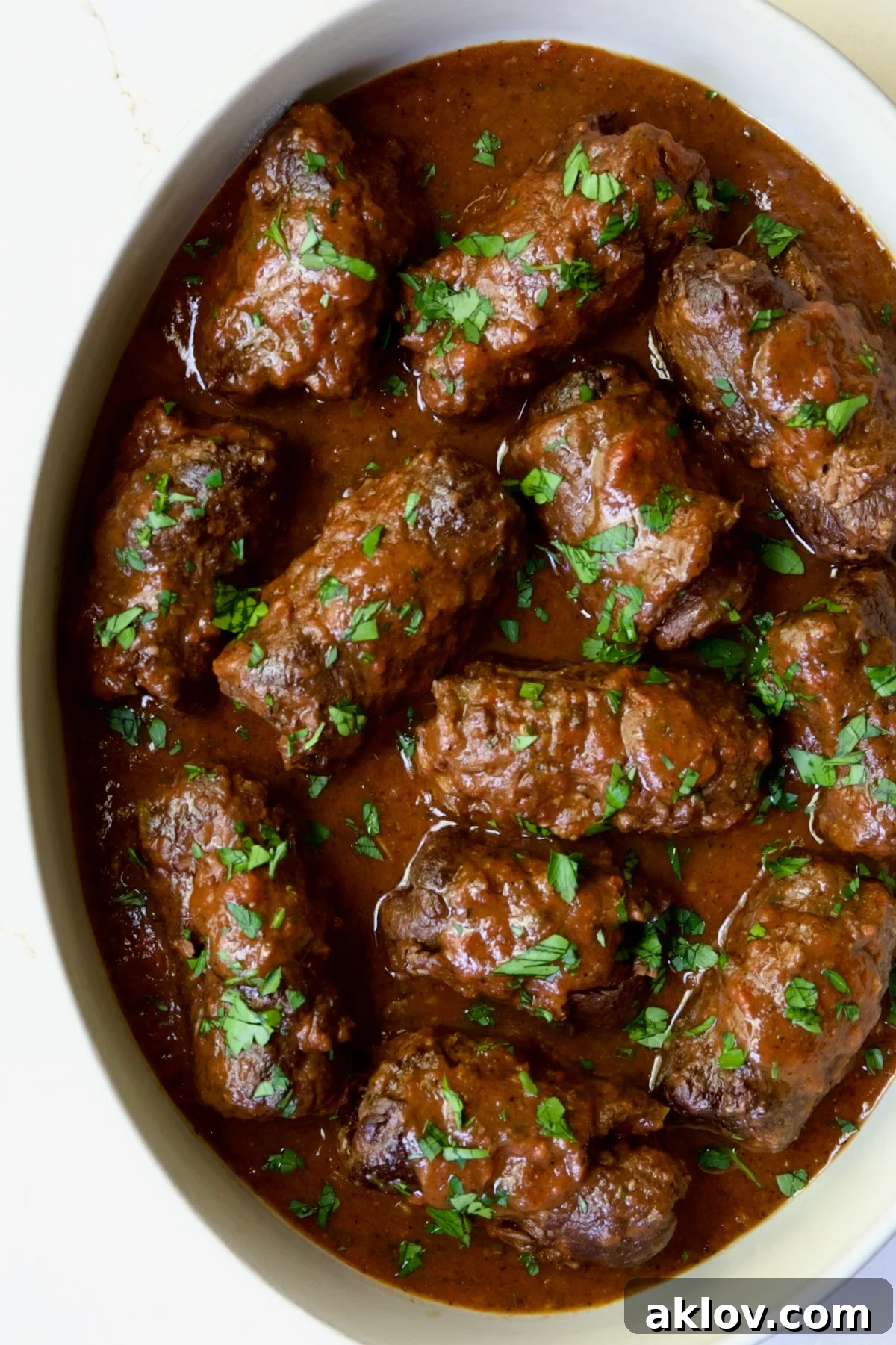 Fully cooked Beef Braciole in white oval dish garnished with fresh parsley.