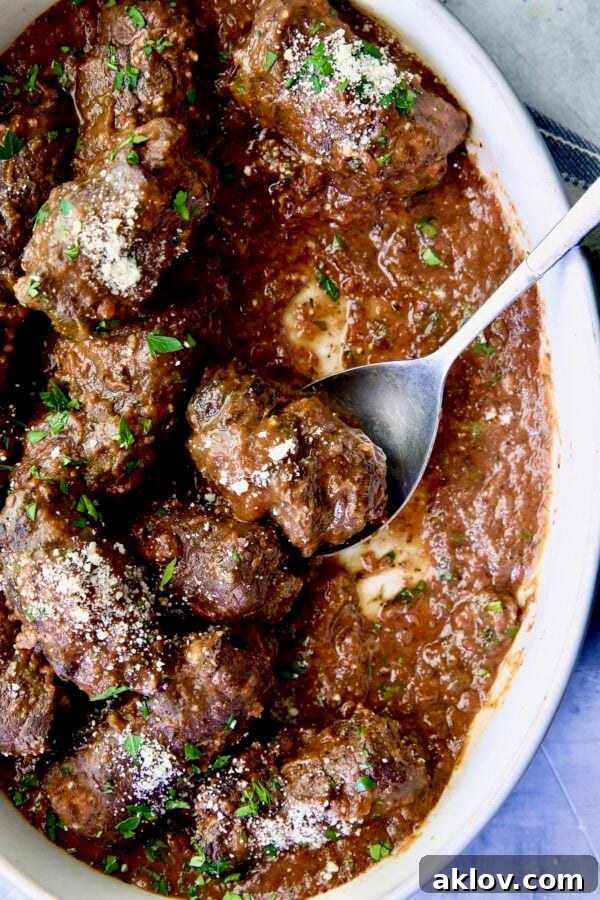 Beef Braciole in oval white serving dish with serving spoon.