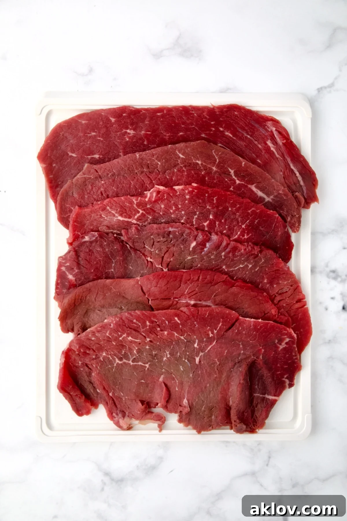 Six slices of beef top round on white plastic cutting board.
