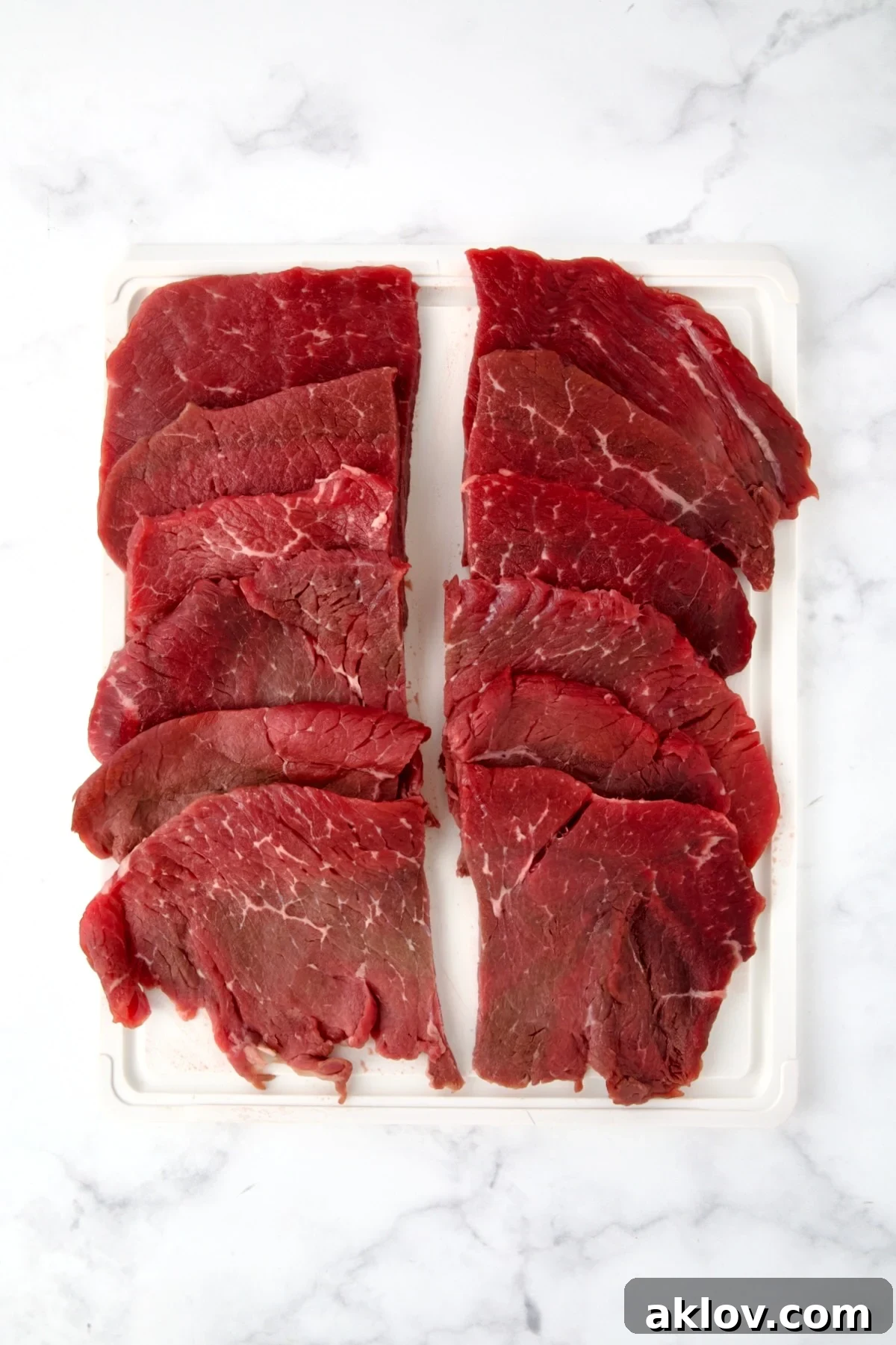 Six slices of beef top round on white plastic cutting board cut in half widthwise to create 12 pieces.