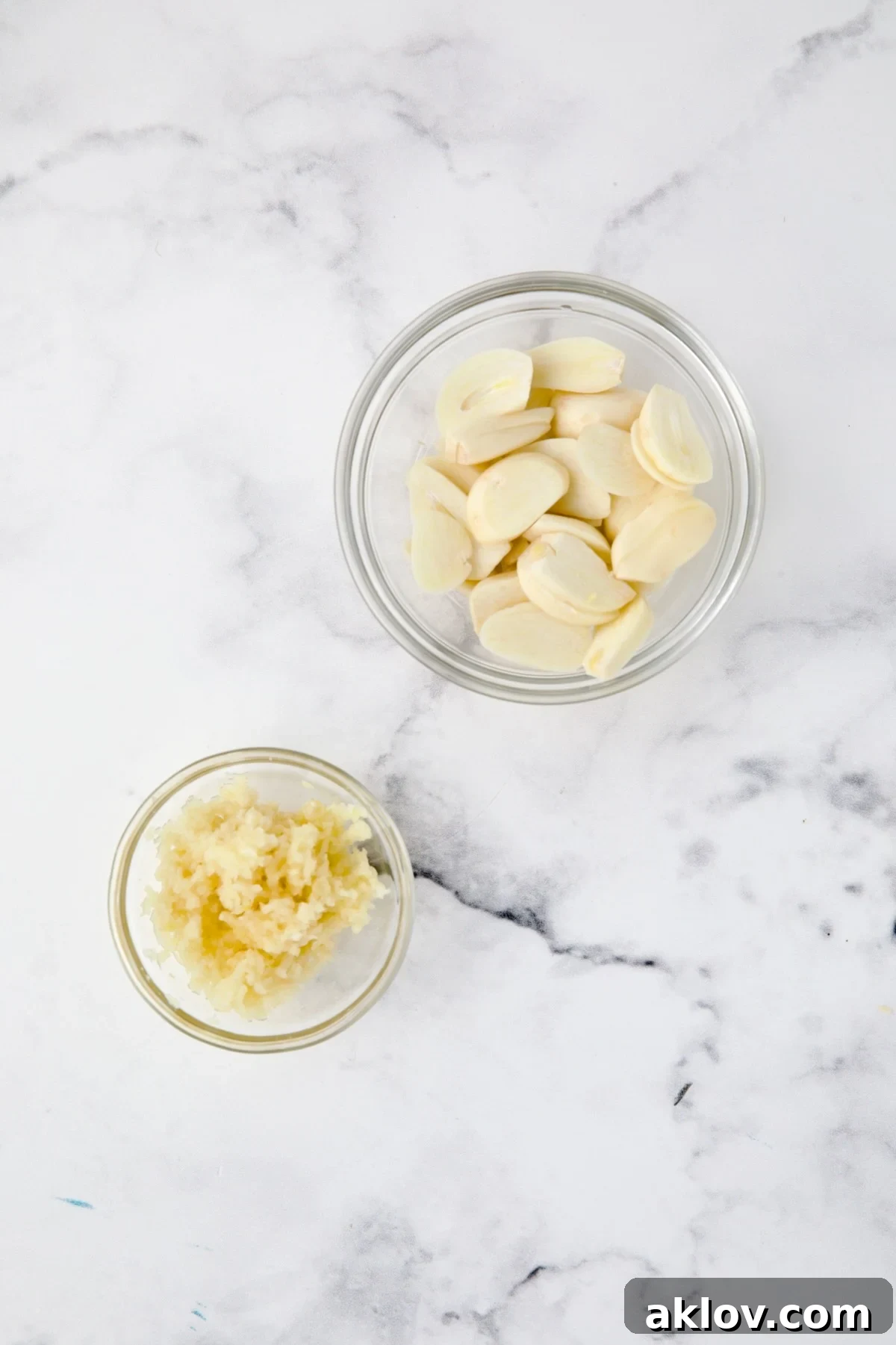 Two glass bowls of garlic with one showing minced and another showing sliced.