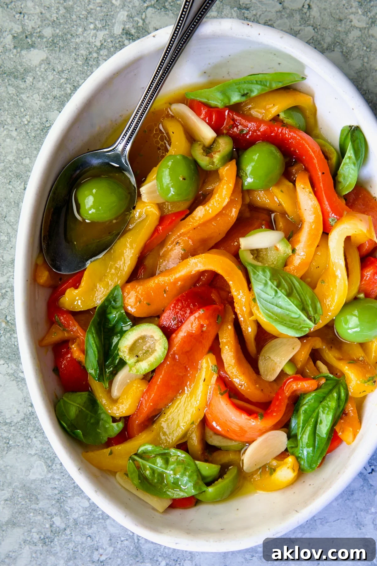Roasted Pepper Salad in white oval serving bowl with serving spoon garnished with fresh basil leaves.