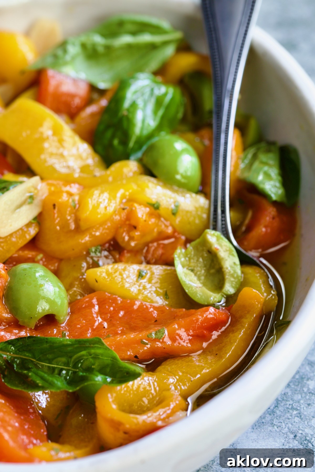 Roasted Pepper Salad in white oval serving bowl with serving spoon garnished with fresh basil leaves.