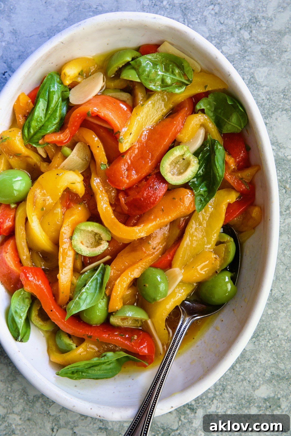 Roasted Pepper Salad in white oval serving bowl with serving spoon garnished with fresh basil leaves.