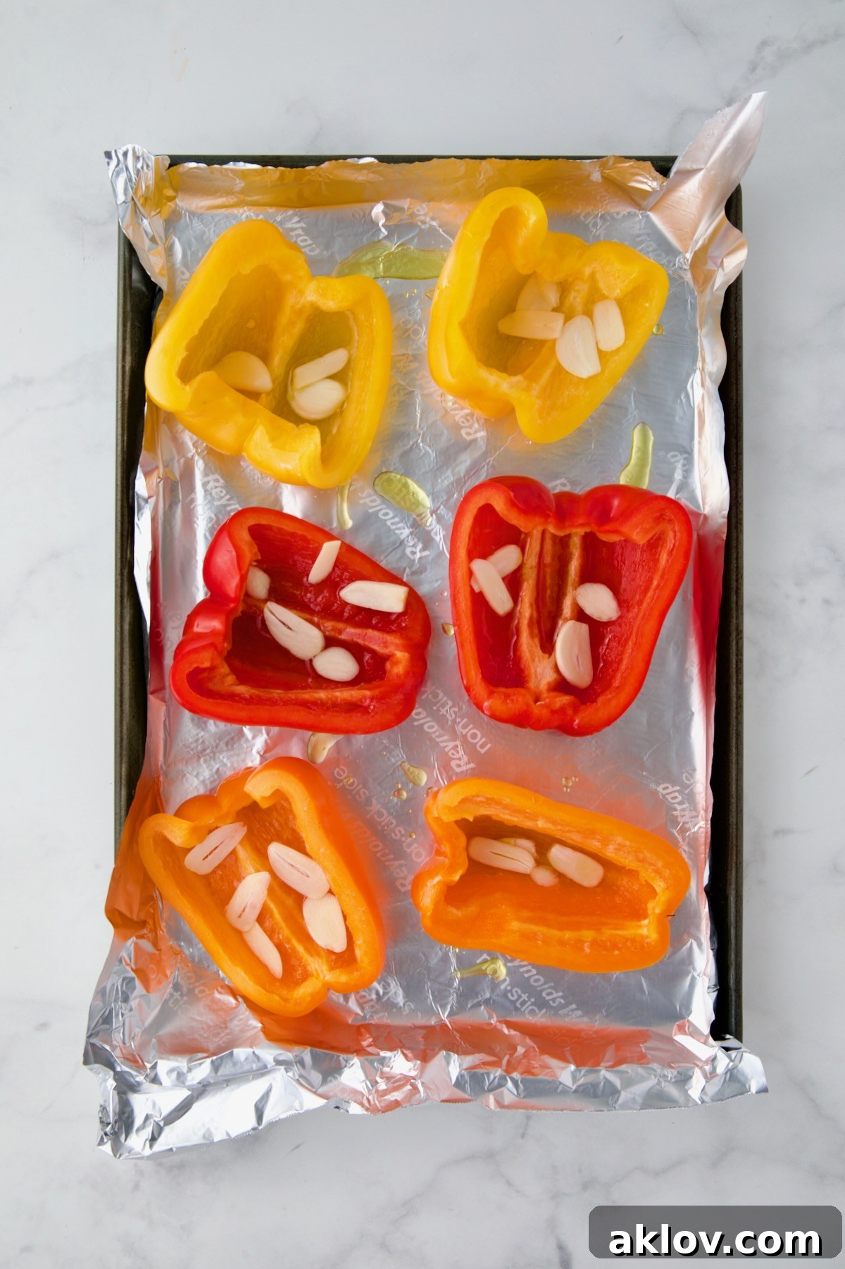 Yellow, red and orange bell pepper halves on aluminum foil-lined rimmed sheet pan with garlic halves in them.