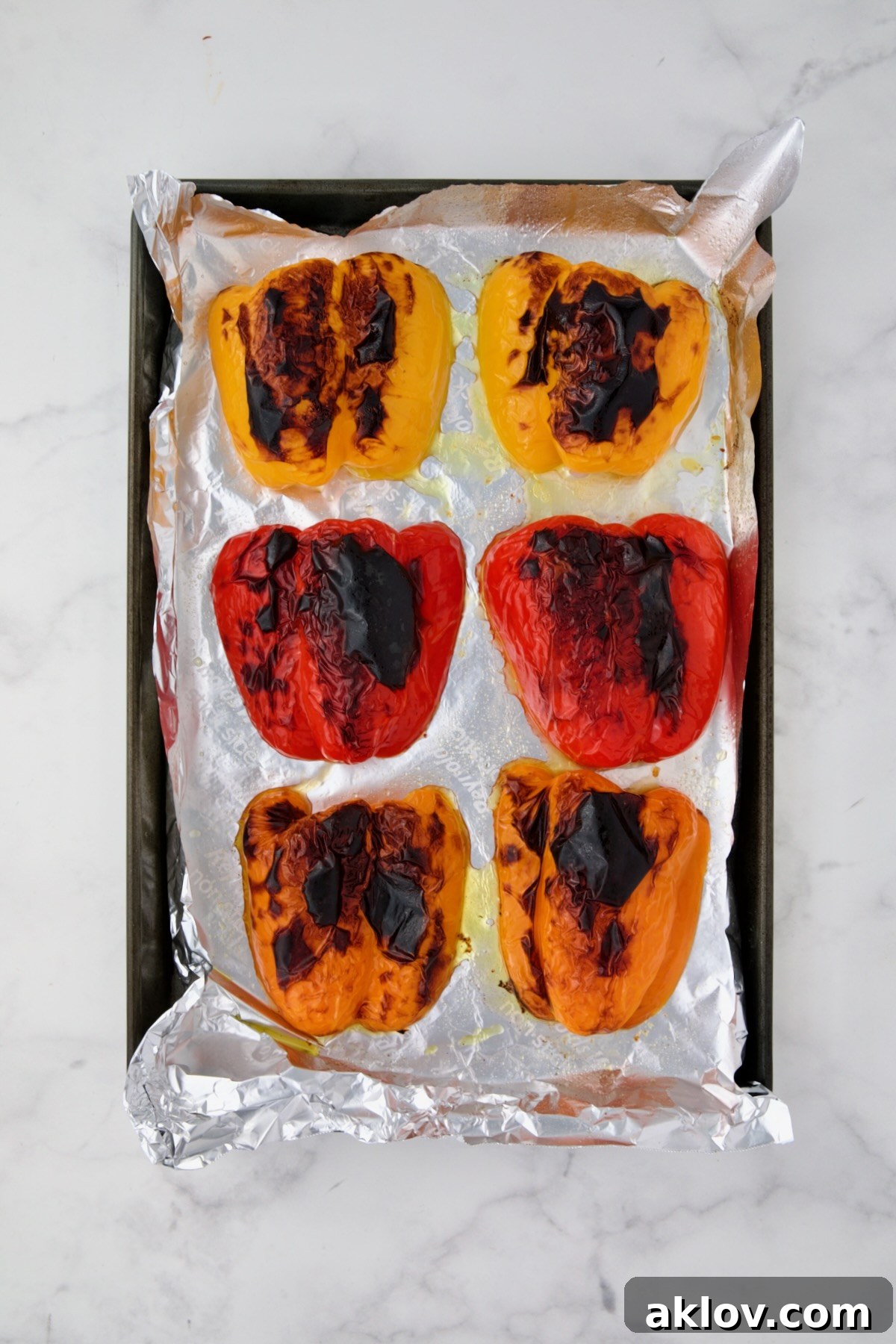 Charred yellow, red and orange bell pepper halves on aluminum foil-lined rimmed baking sheet.