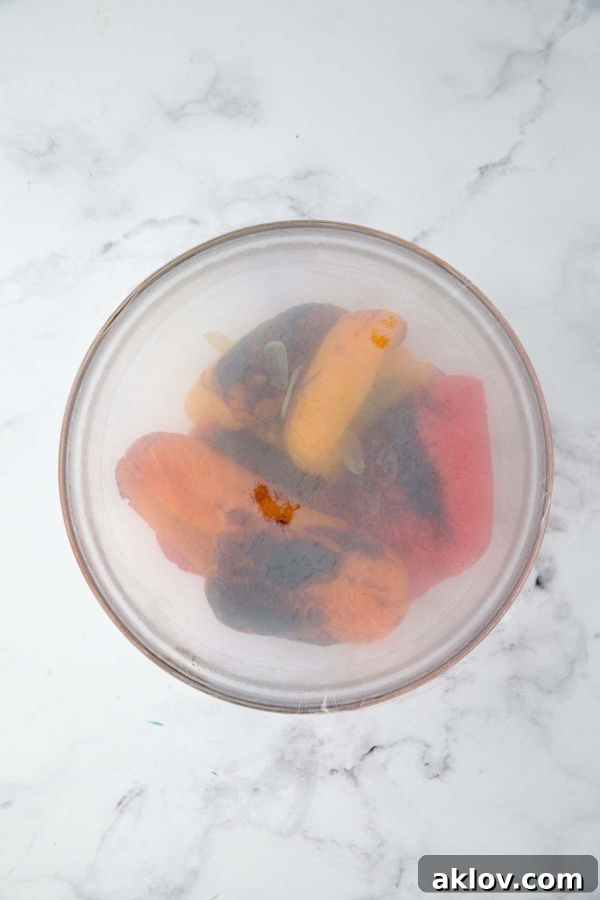 Roasted bell pepper halves in glass bowl with plastic wrap over it for the peppers to steam.