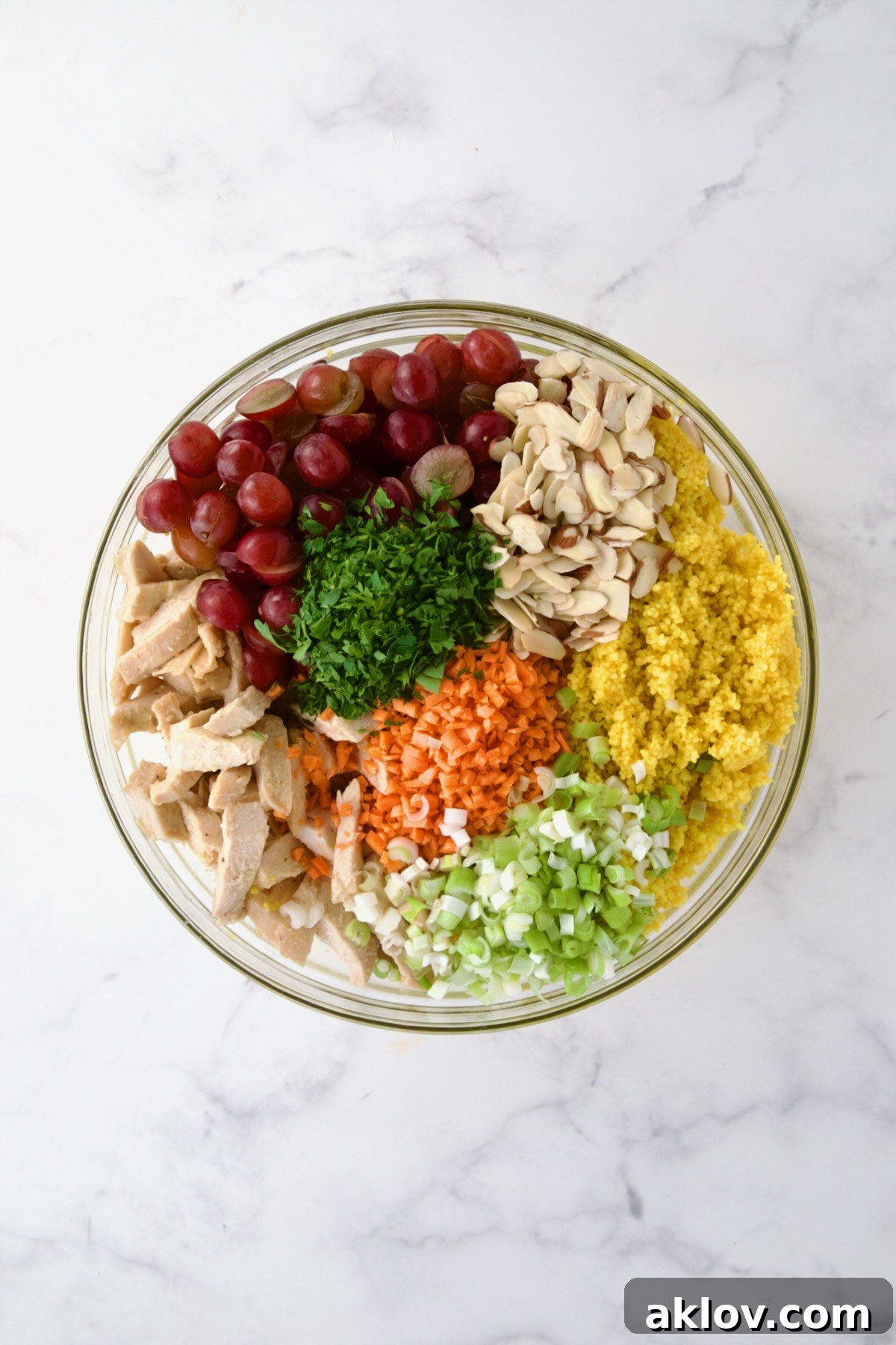 A large glass bowl holding various ingredients for the Chicken Couscous Salad, including chicken, couscous, and fresh vegetables, before being fully combined.