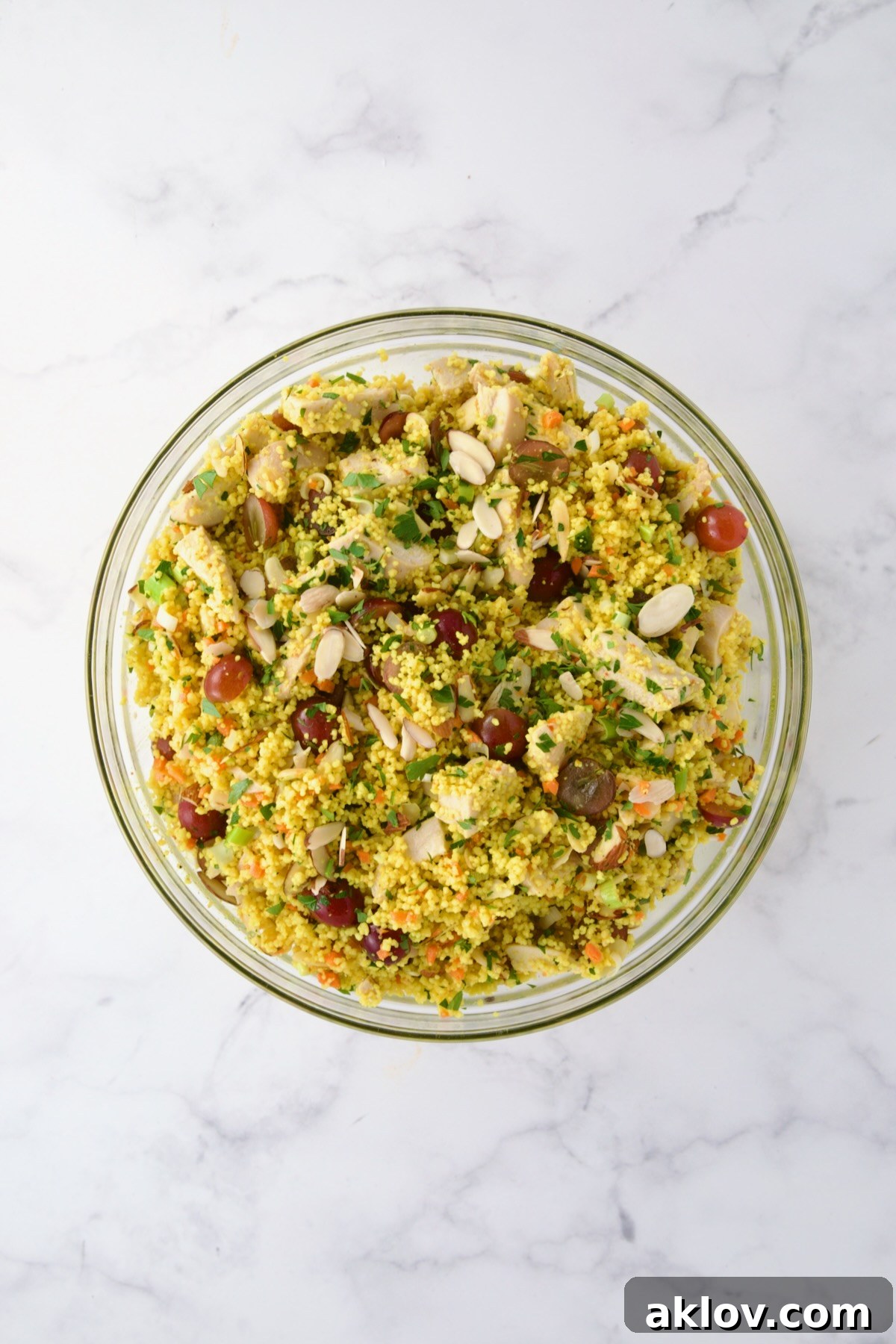 The vibrant ingredients for Chicken Couscous Salad, including chicken, couscous, scallions, carrots, grapes, almonds, and parsley, perfectly combined in a large glass bowl.