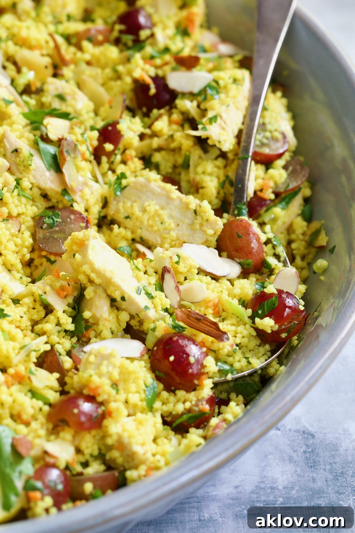 A prepared Chicken Couscous Salad in a gray bowl, with a serving spoon, showcasing its readiness to be enjoyed.