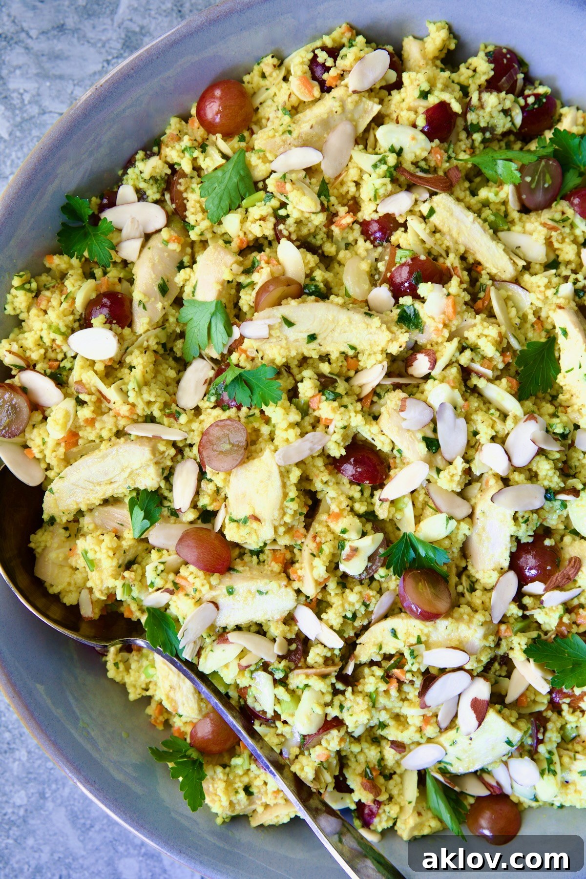 A refreshing Chicken Couscous Salad, presented beautifully in a gray bowl with a serving spoon, inviting you to enjoy its fresh flavors.
