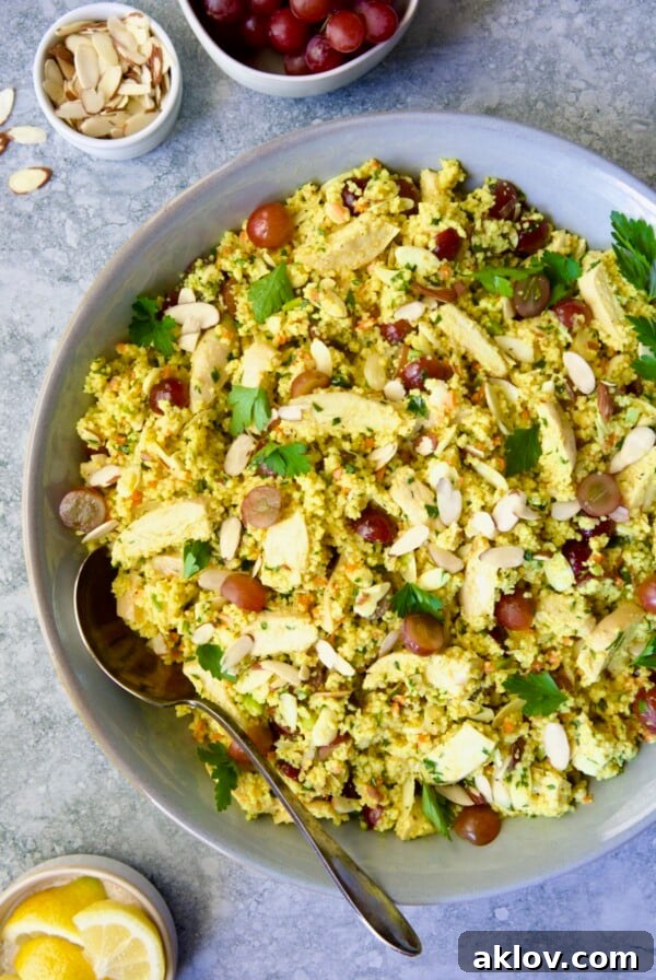 Chicken Couscous Salad in gray bowl with serving spoon with bowl of sliced almonds, whole grapes and lemon wedges.