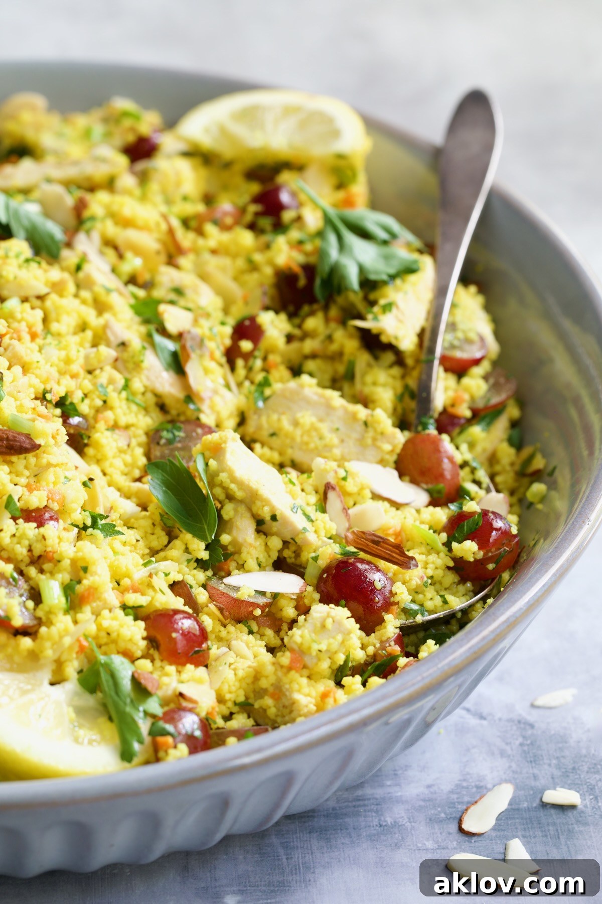 A close-up shot of the vibrant Chicken Couscous Salad nestled in a gray bowl, with a serving spoon ready to dish out its fresh ingredients.
