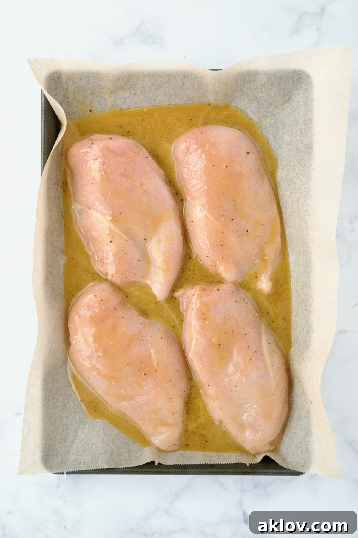 Four uncooked chicken breast halves arranged on a parchment paper-lined baking sheet, generously coated with a savory honey-mustard mixture.