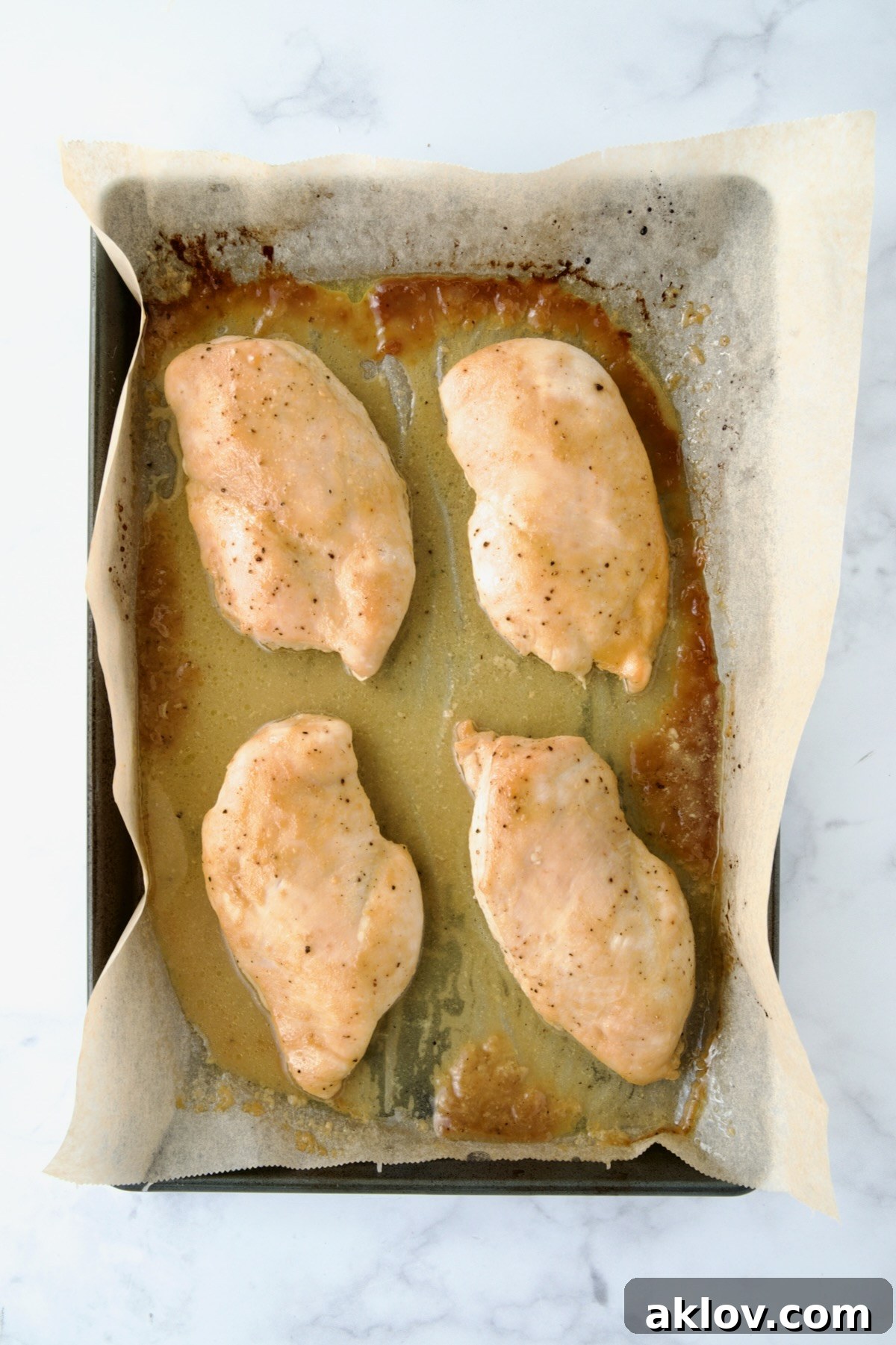 Four perfectly cooked, golden-brown chicken breast halves resting on the parchment paper-lined baking sheet, ready for cooling and slicing.