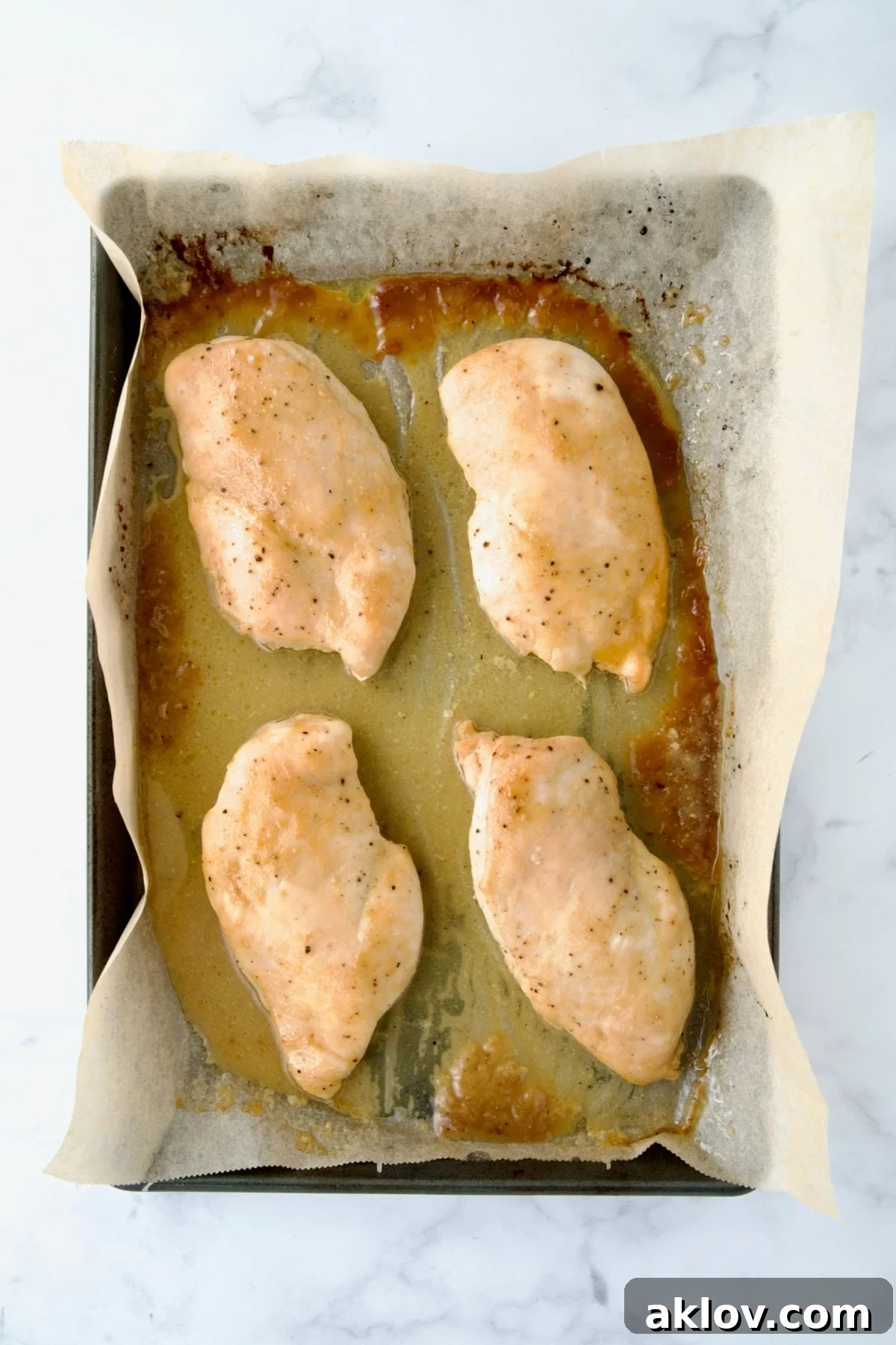Four cooked chicken breast halves on parchment paper lined rimmed baking sheet.