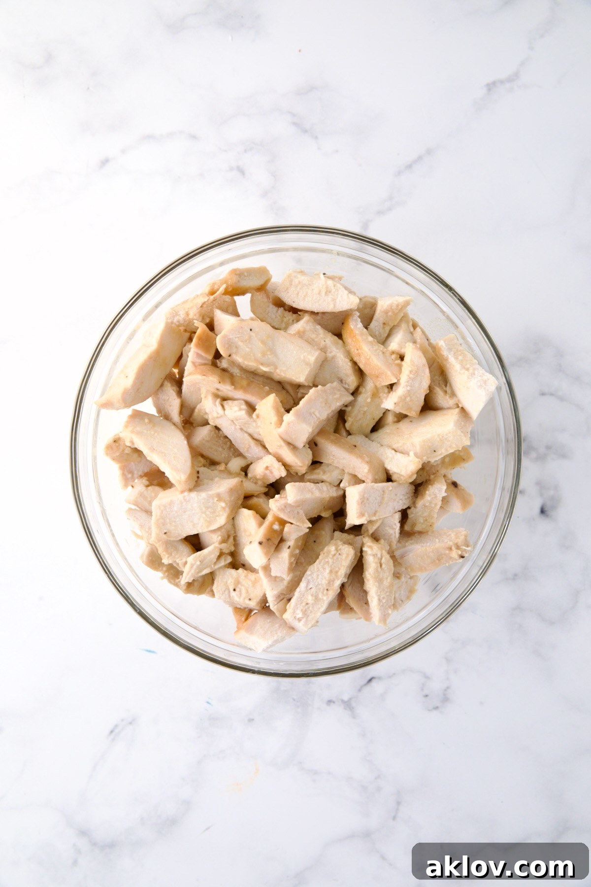 An inviting glass bowl filled with neatly cut pieces of tender, cooked white meat chicken, prepared for the salad assembly.