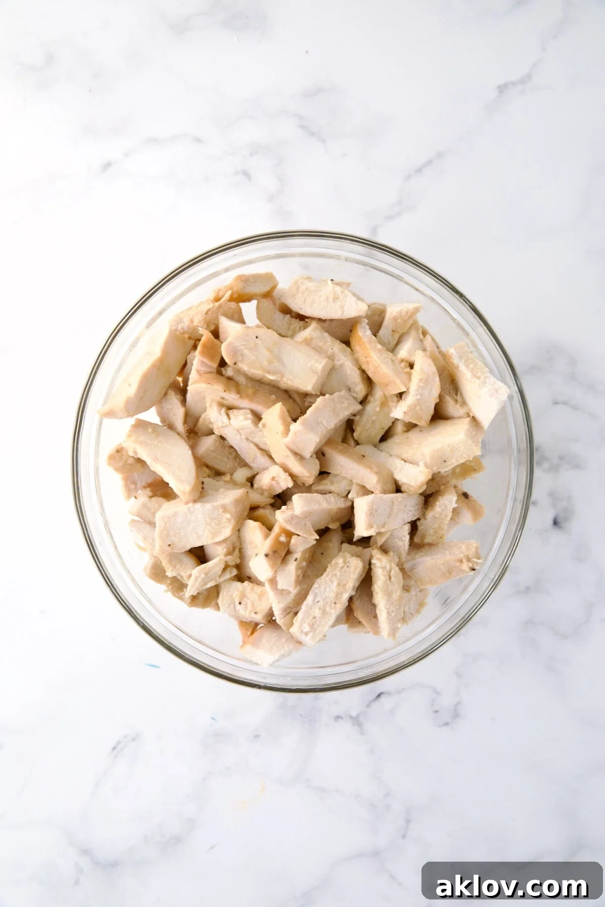 Pieces of cooked white meat chicken in glass bowl.