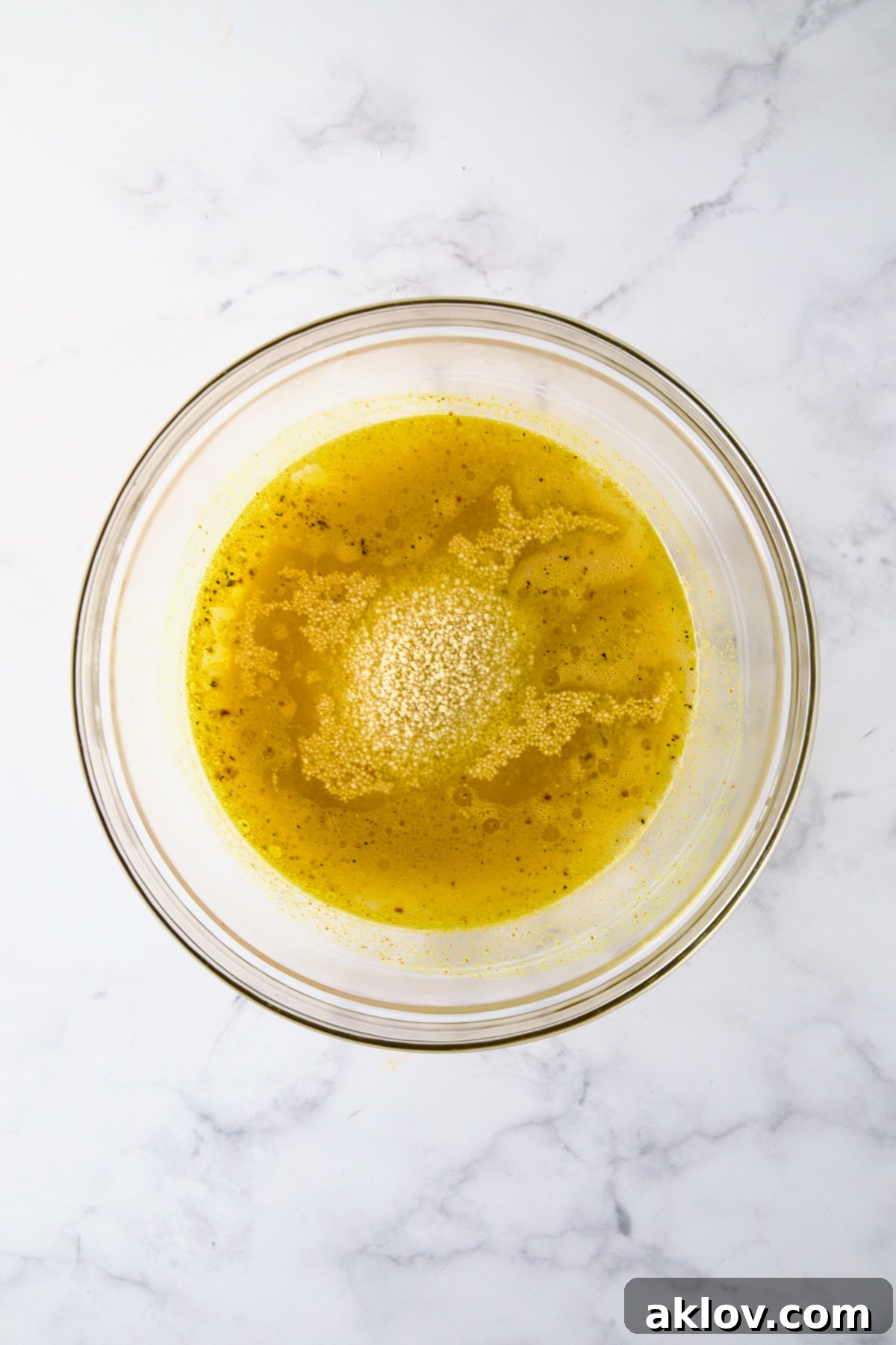 Dry couscous grains being added to a glass bowl containing seasoned boiling water, beginning the hydration process.