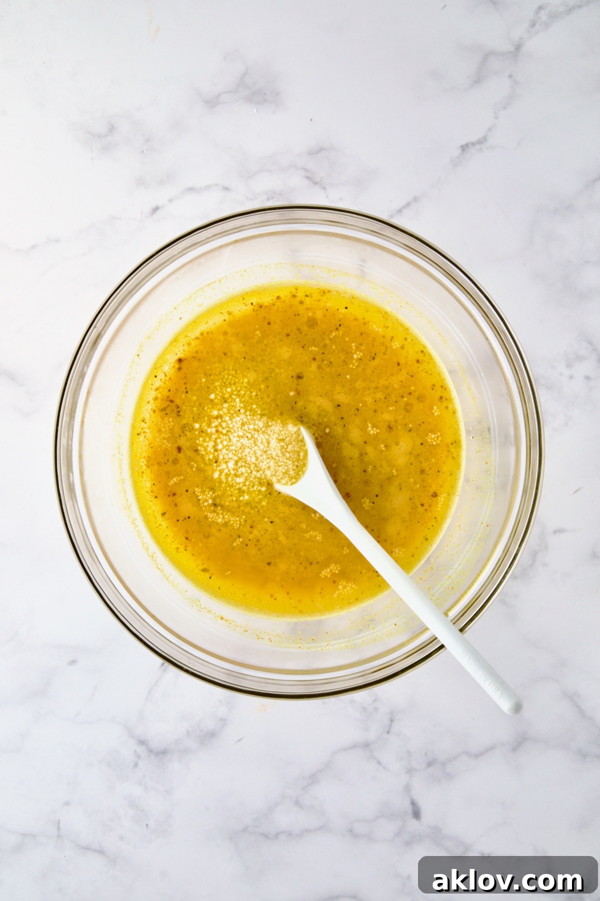 Uncooked couscous being gently stirred into the seasoned water in a glass bowl with a white mixing spoon, ensuring even distribution.