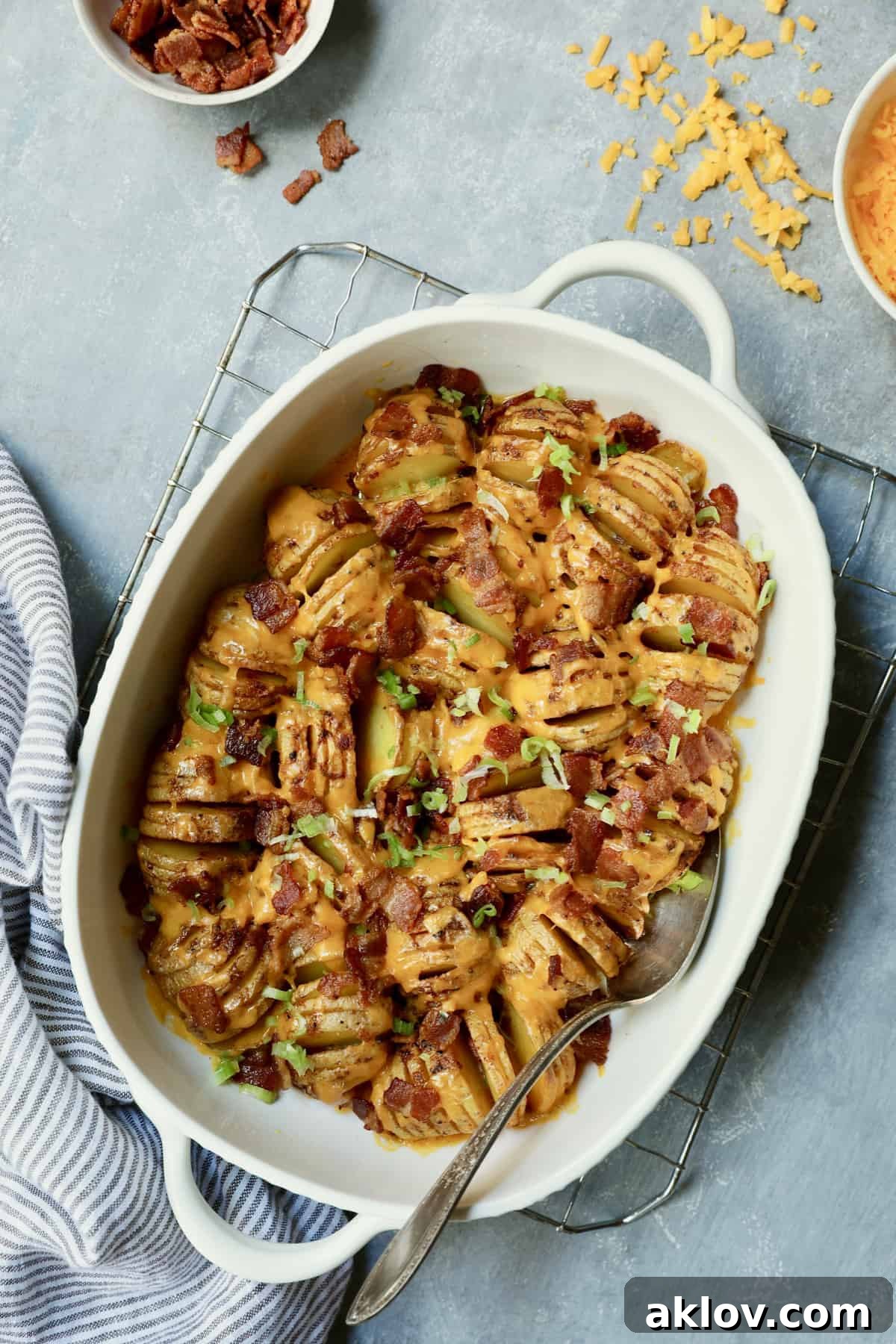 Photo of Baby Hasselback Potato Bake with Cheddar and Bacon on cooling rack with bacon and cheese scattered about.