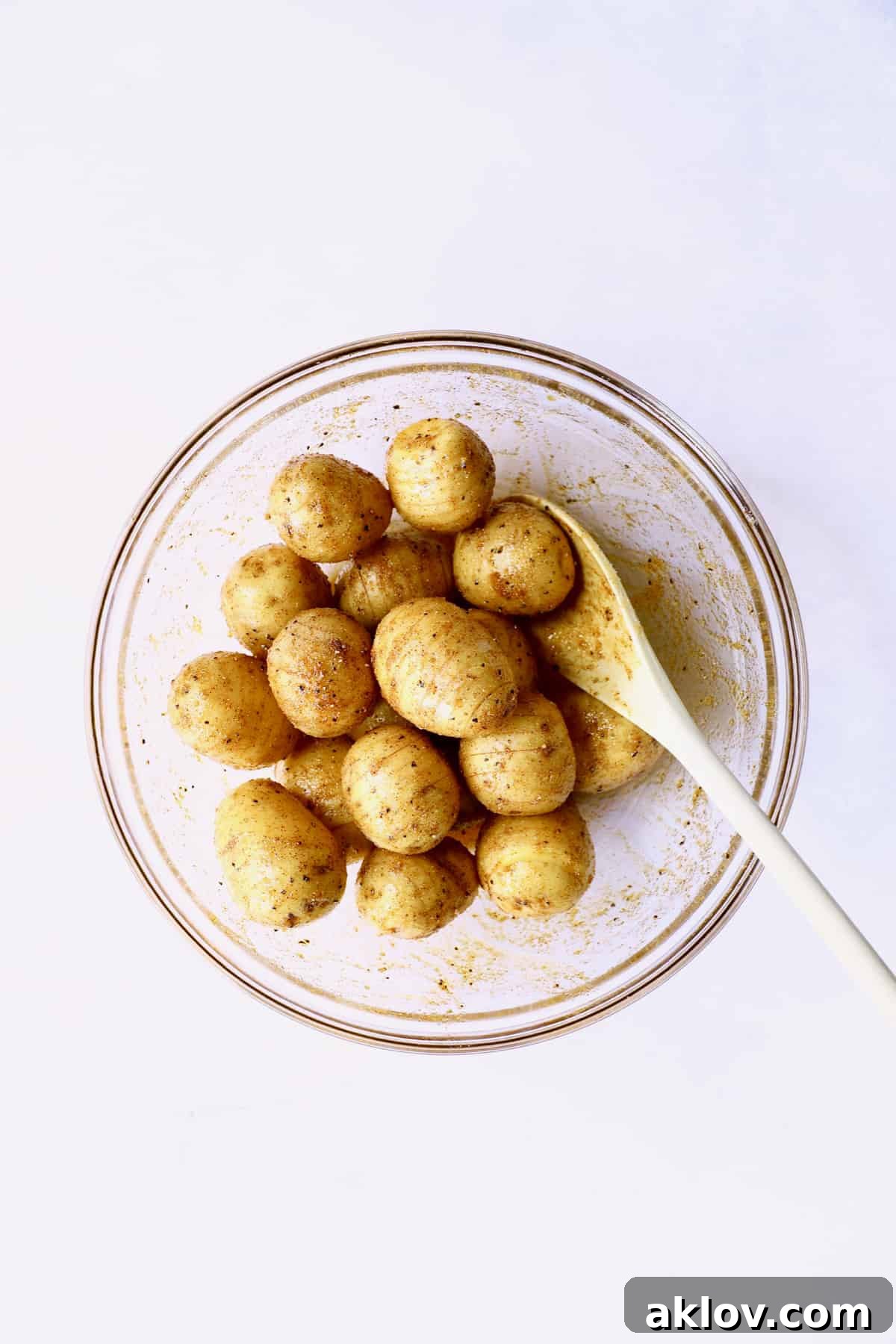 Photo of Yukon gold potatoes in glass bowl being tossed with oil and spices.