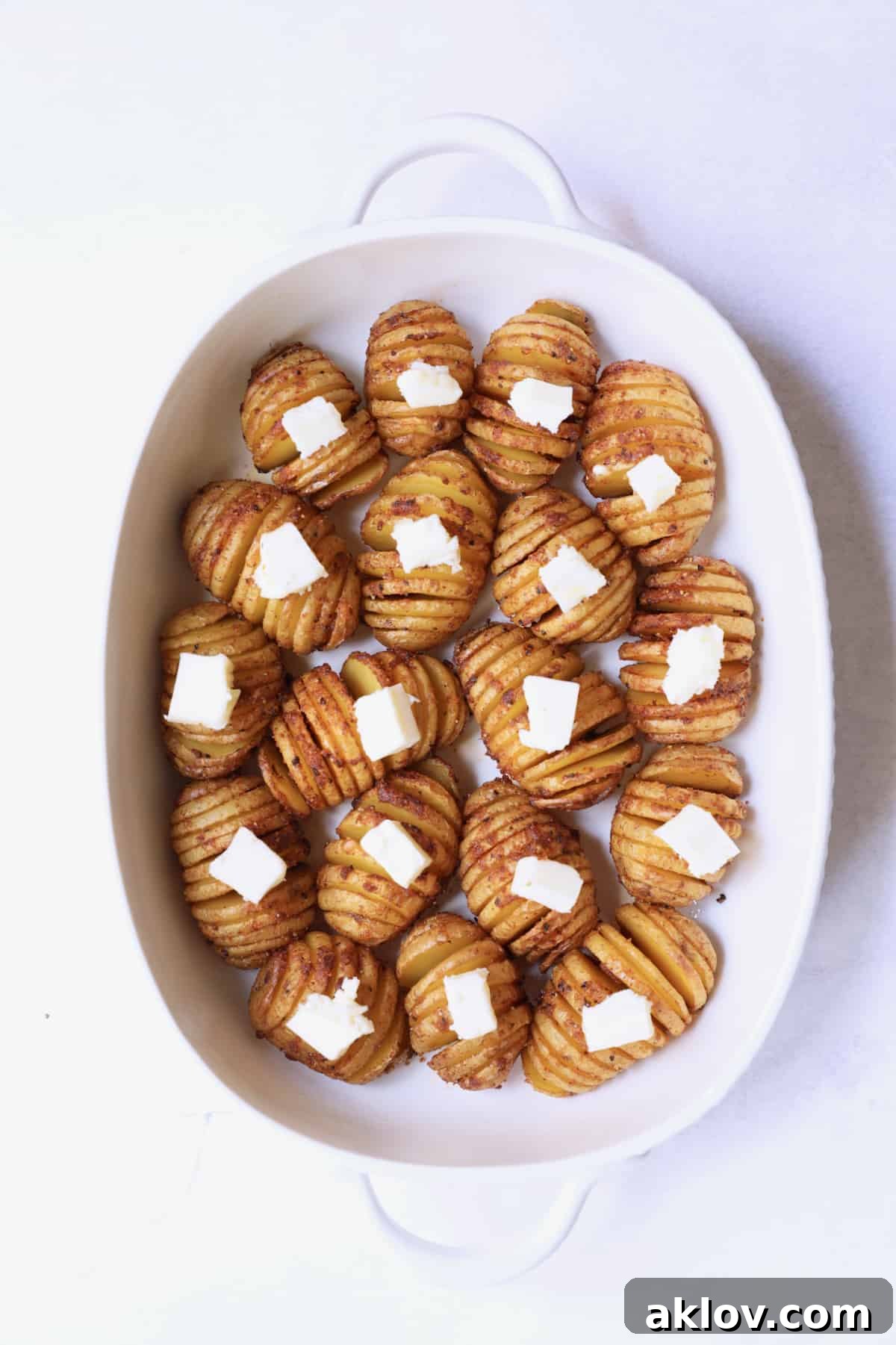 Photo of roasted hasselbacked potatoes in white baking dish dotted with butter.