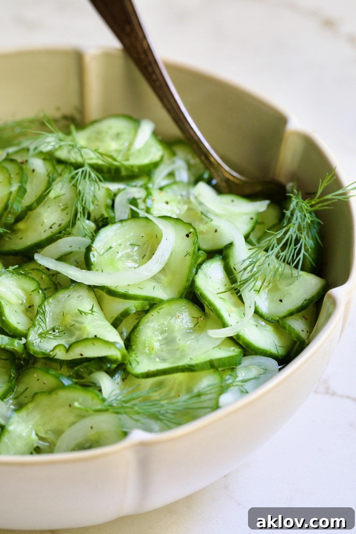 Serving of Cucumber Onion Salad in a bowl with a silver serving spoon, ready for a meal.