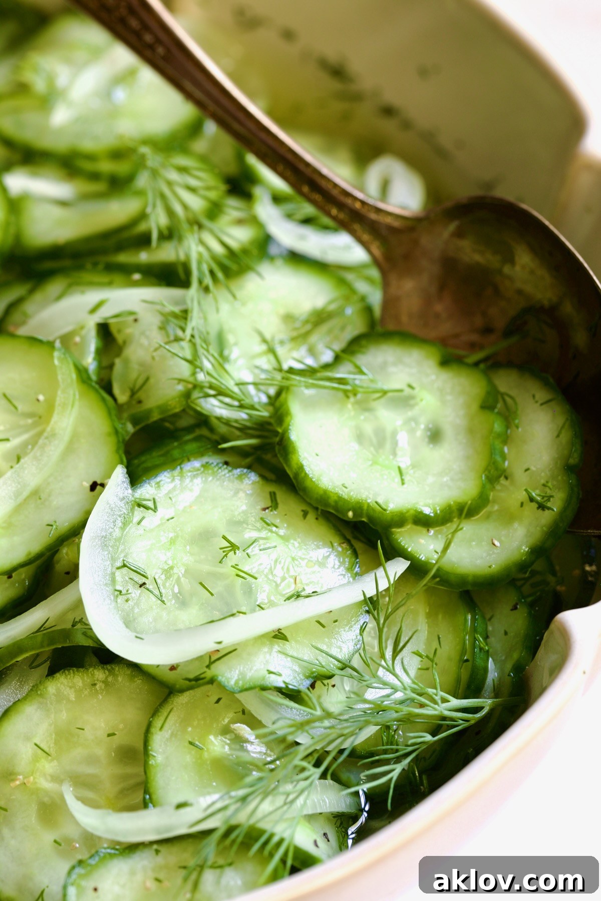 Cucumber Onion Salad in a white serving bowl with a wooden serving spoon.