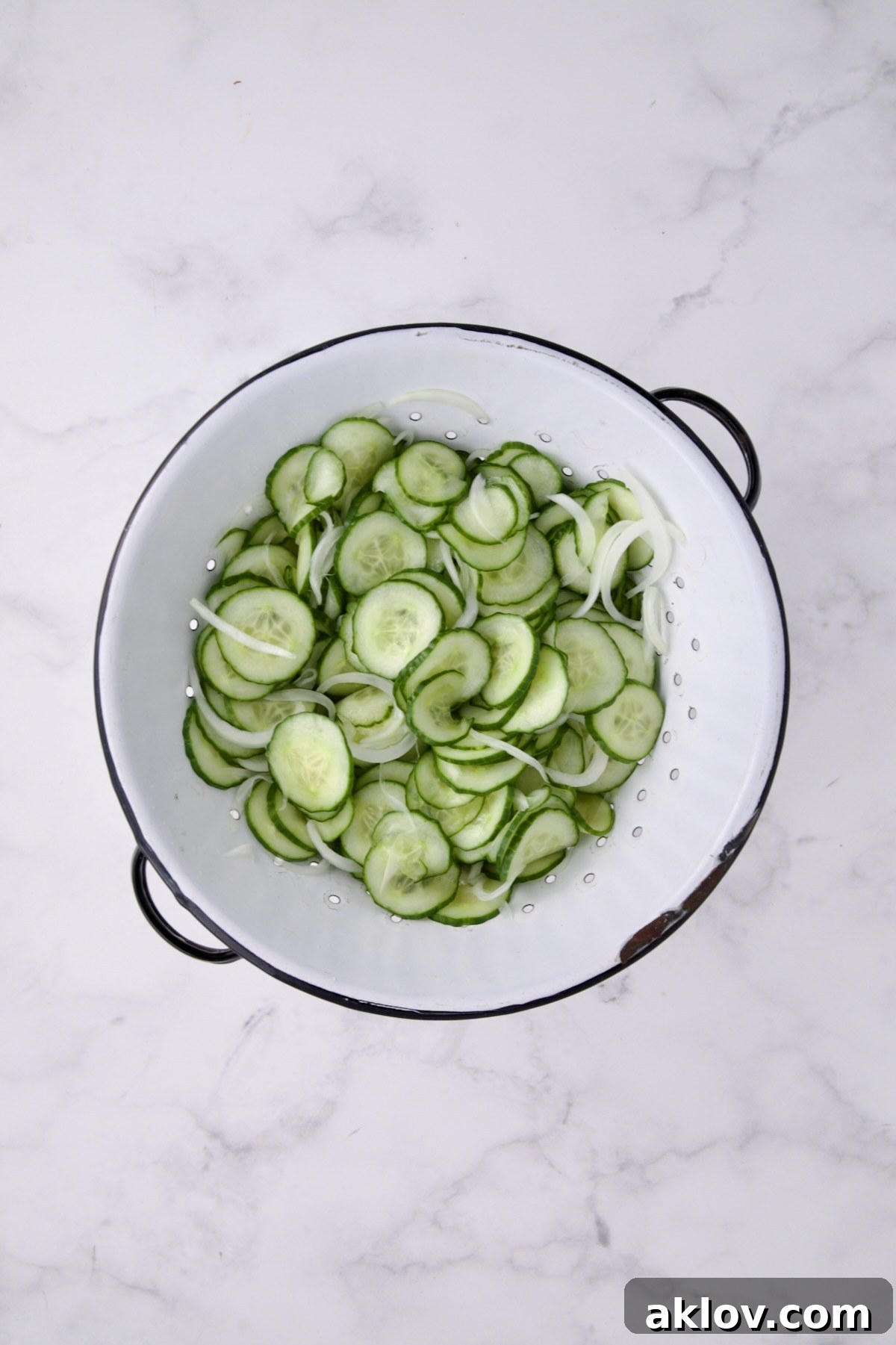 Salted and drained cucumbers and onions in a white distressed colander.