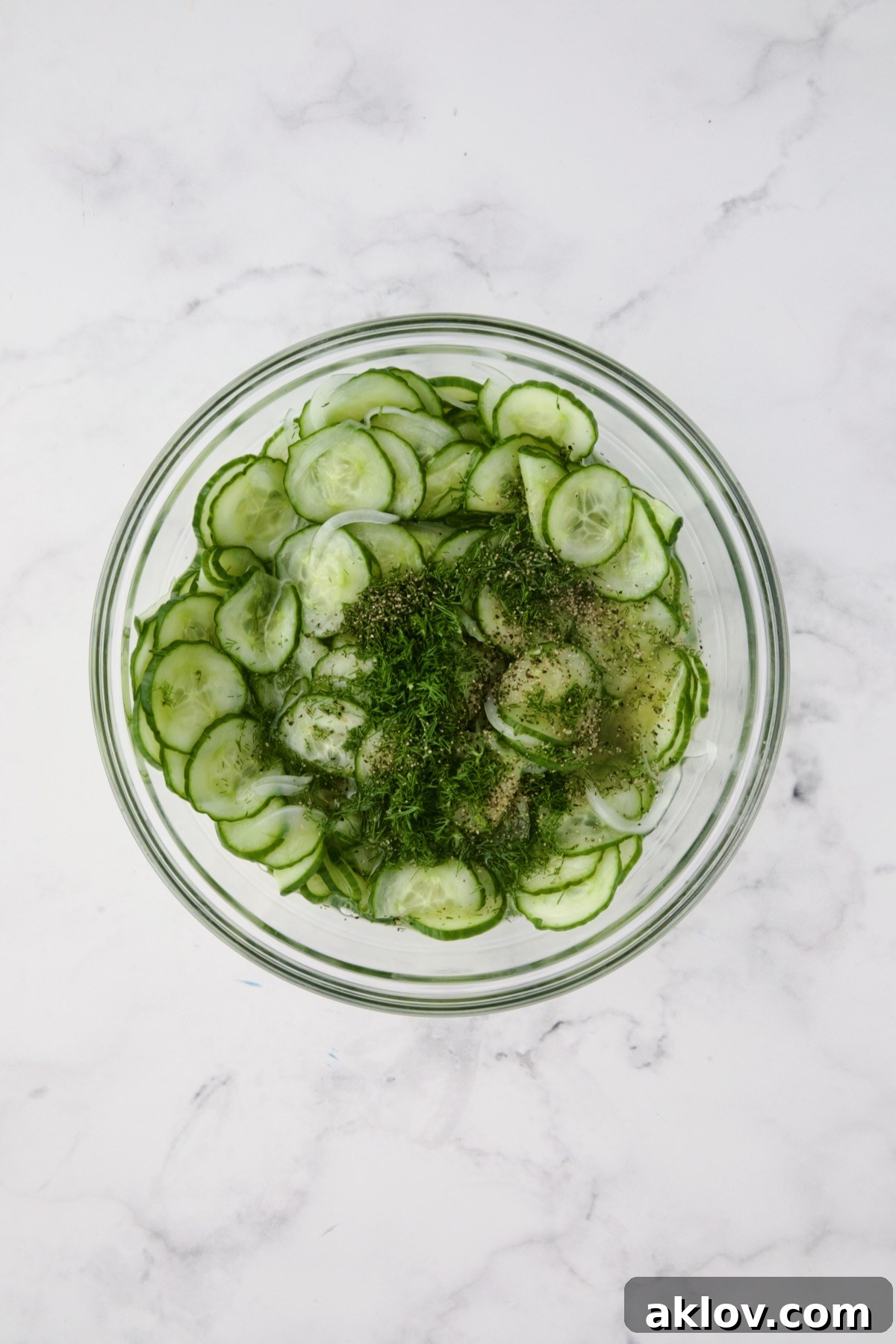 Cucumbers, onions, dressing, and fresh dill combined in a glass bowl before final mixing.