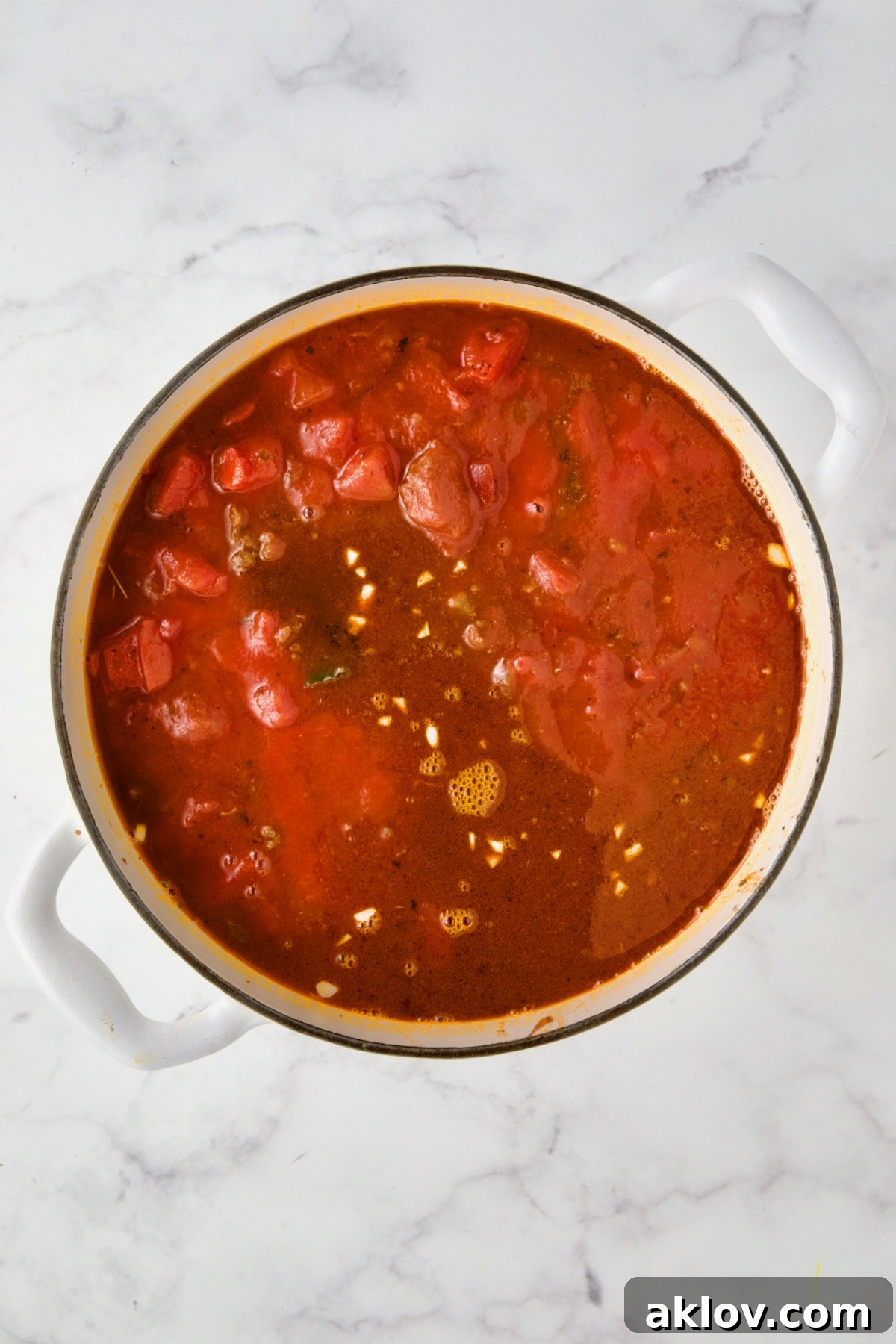Tomatoes, tomato sauce and beef broth added to white enamel Dutch oven.
