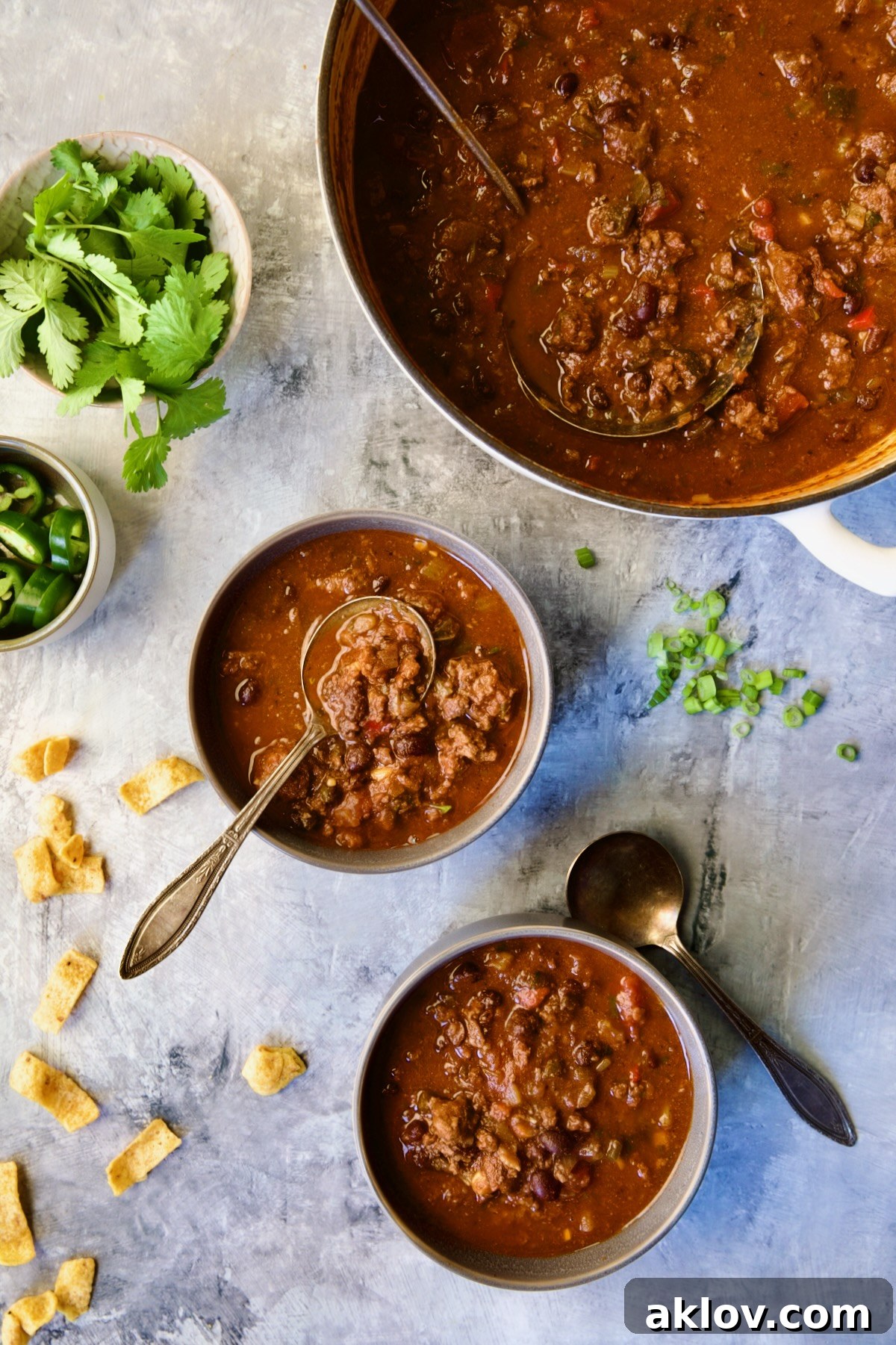 Beef and Chorizo Chili being dished up from white enamel Dutch oven into two gray bowls.